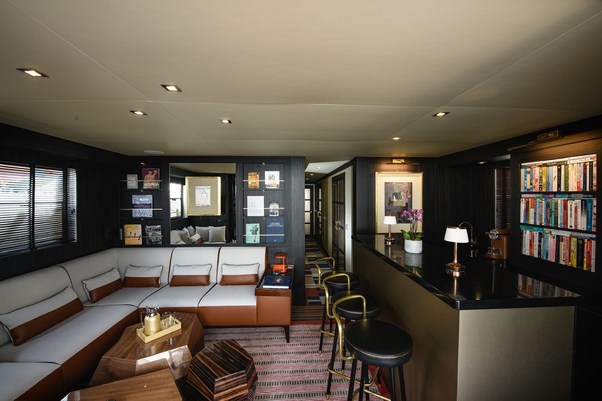 Luxurious modern yacht interior with sofa, bar, bookshelves, and artworks.