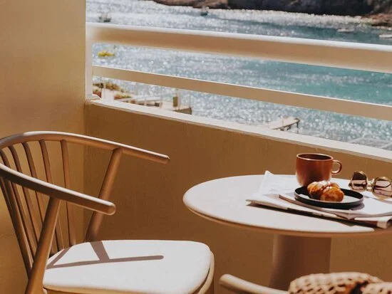 Balcony with table, chair, croissant, coffee, and sea view.