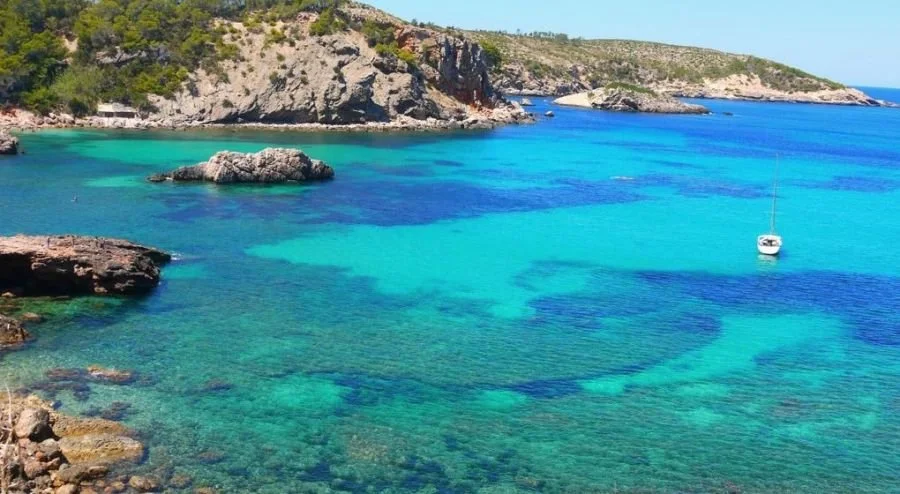 Coastal landscape with turquoise water, rocky cliffs, and a small boat in the bay.