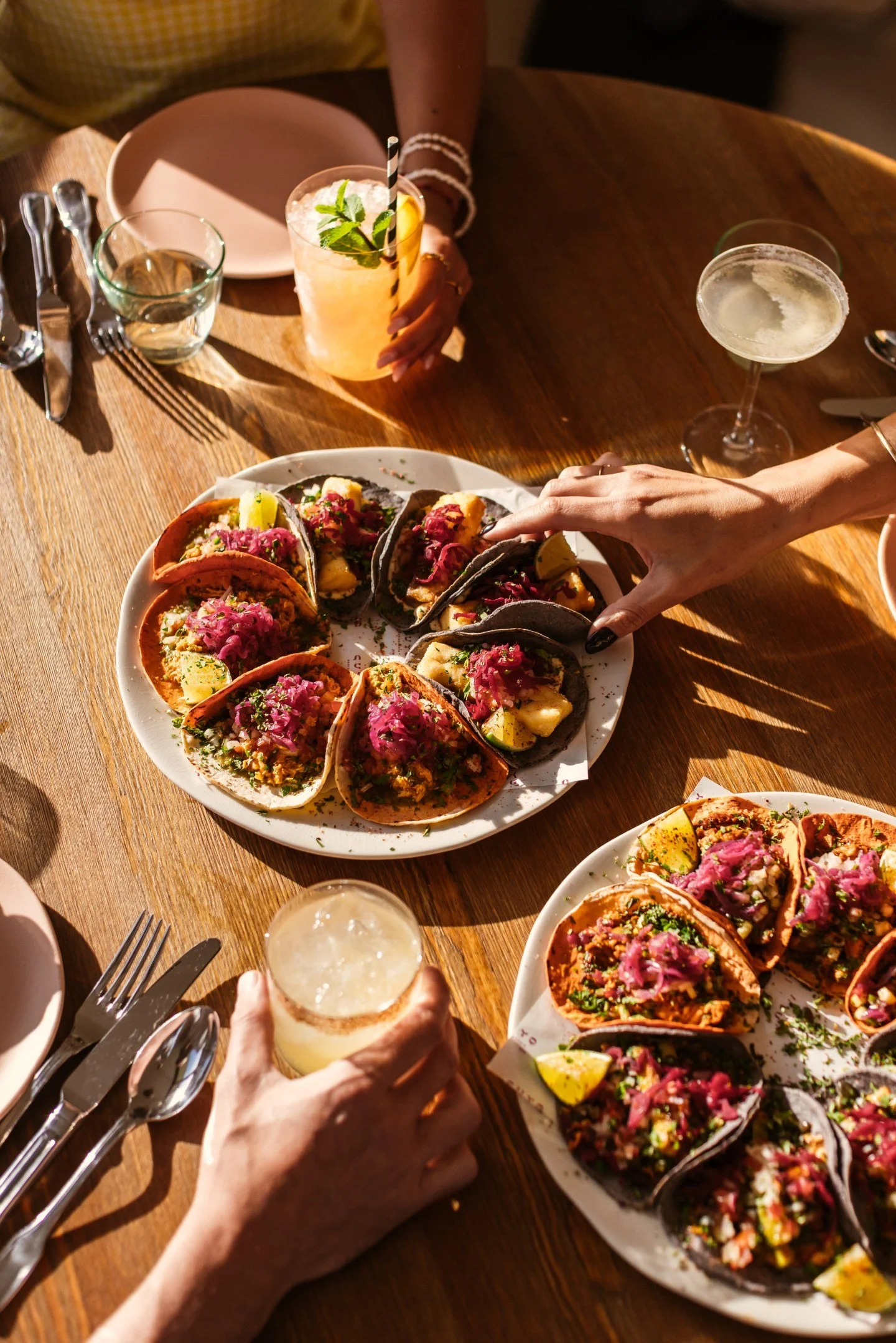 Plates of colorful tacos with drinks on a wooden table