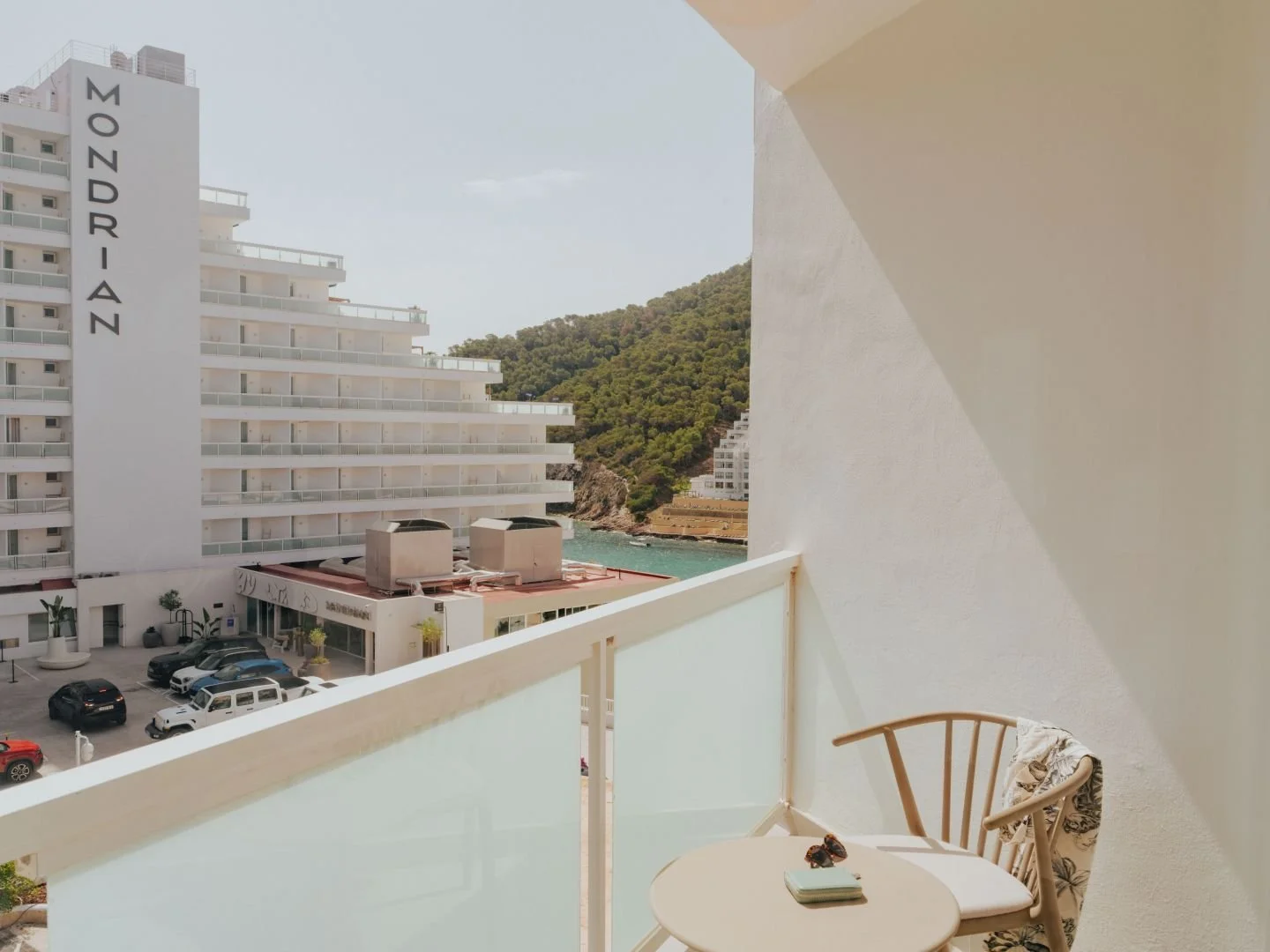 View from a balcony with a table and chair, overlooking a hotel named 'Mondrian' and a scenic coastal landscape.