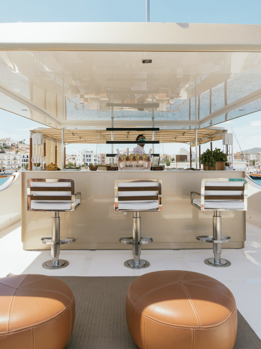 Luxury yacht bar with stools and champagne bottles, outdoor setting in port, sunny day.