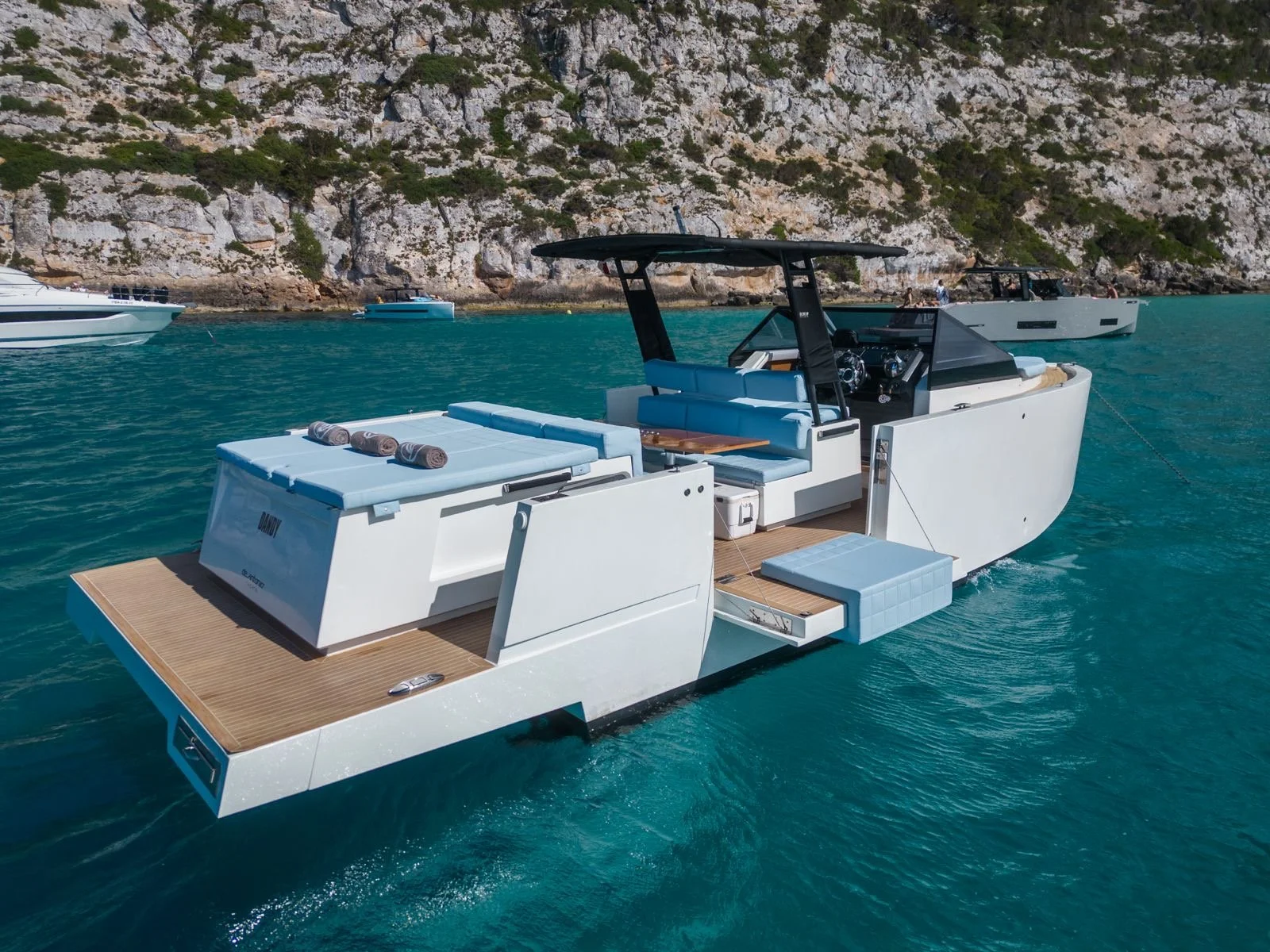 Luxury motor yacht anchored in turquoise sea near rocky coastline, featuring sleek design and sunbathing area.