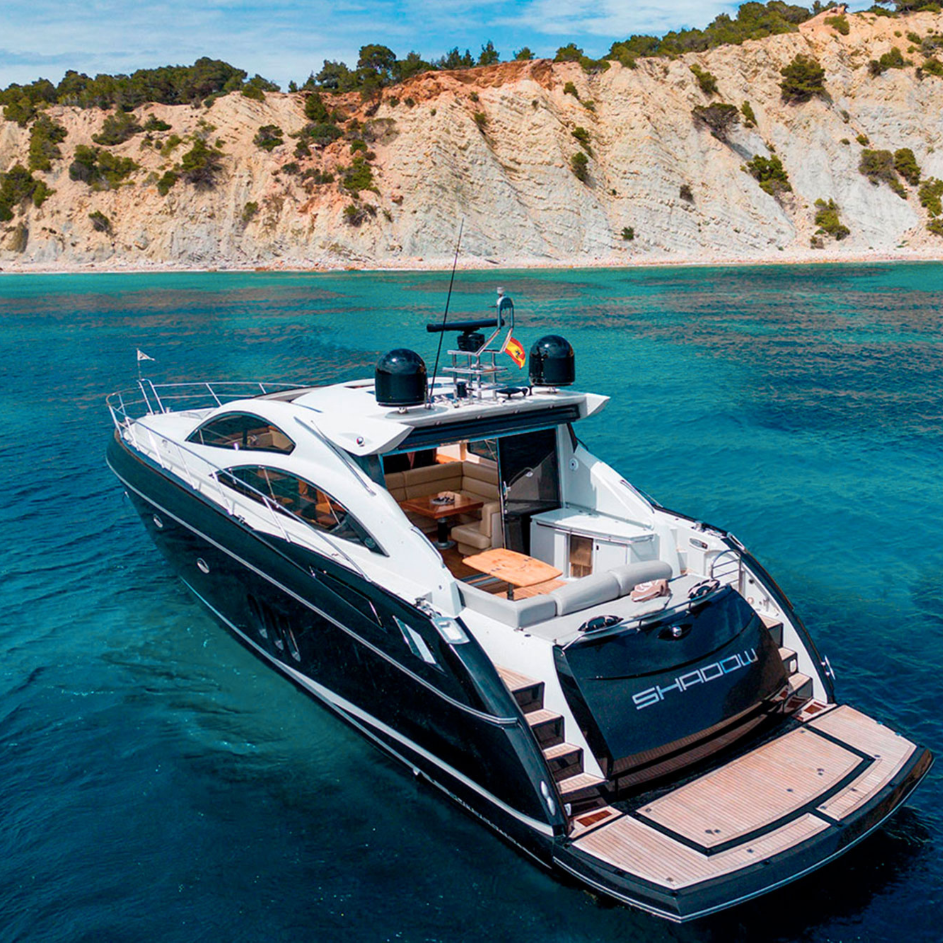 Luxury yacht anchored near a rocky coastline with clear blue water.