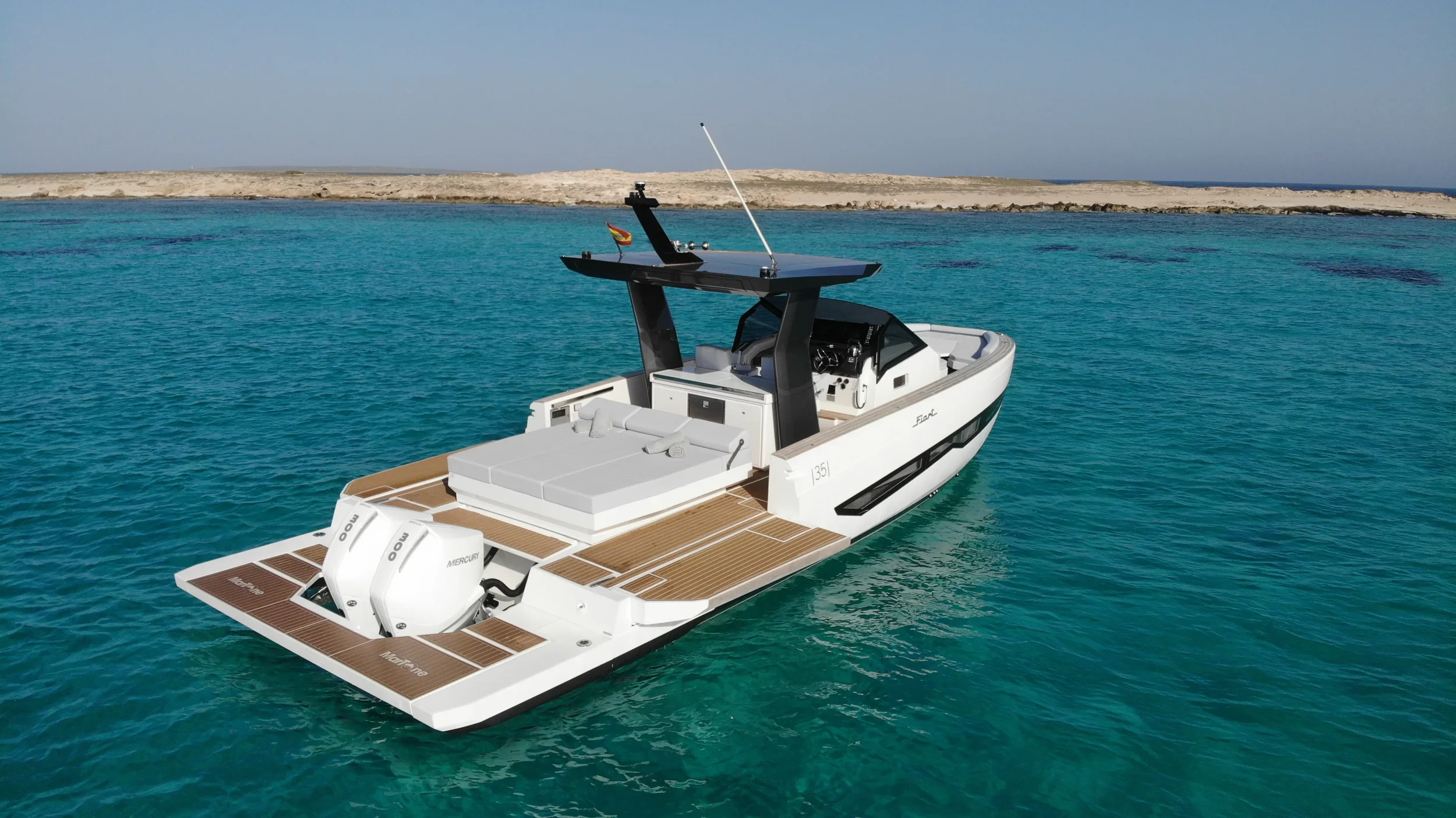 Side view of the Fiart 35 Martone W anchored near the coastline with the wide teak platform and bow lounge in sight.
