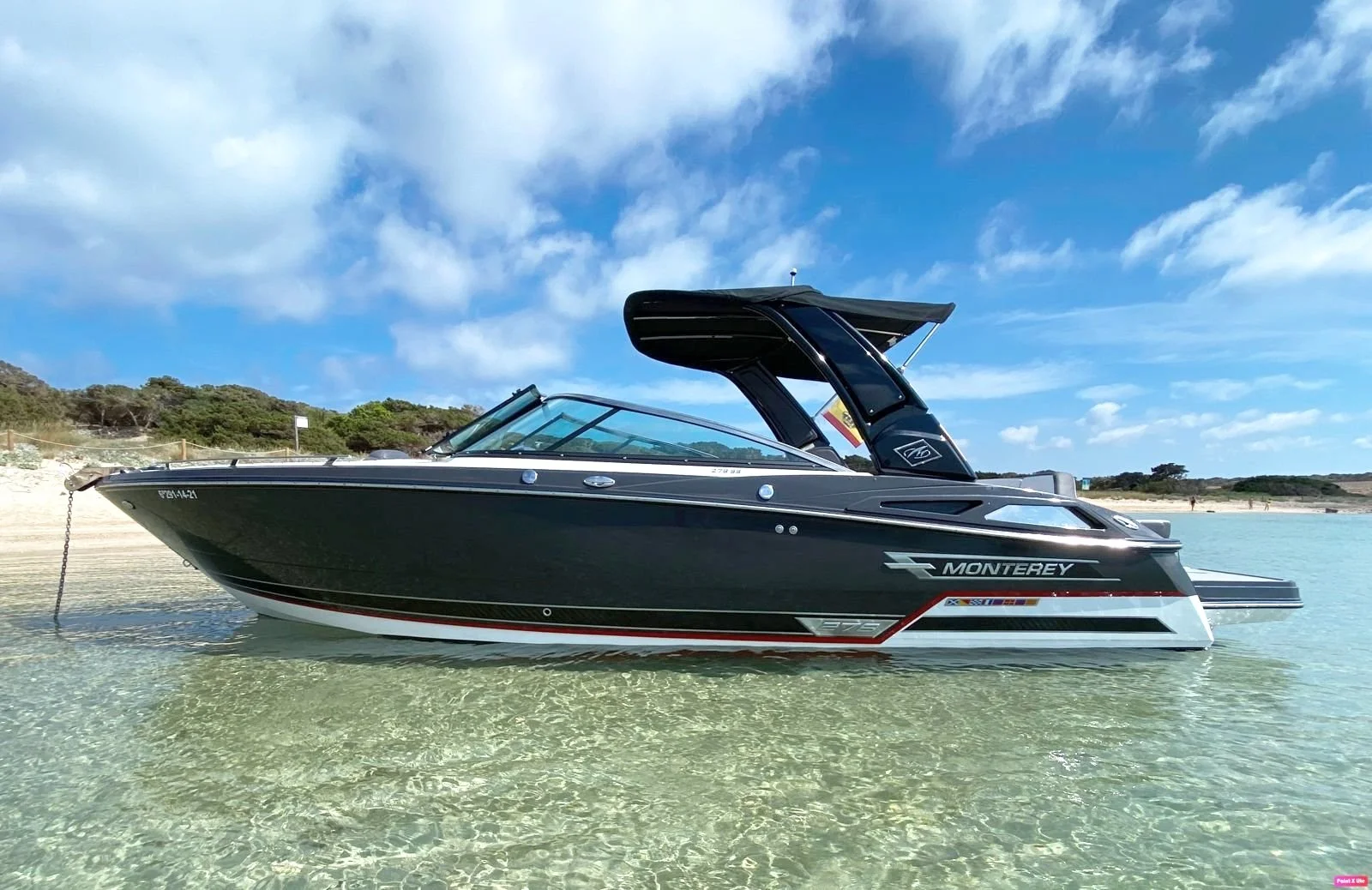 Monterey motorboat in clear water near a sandy beach with blue sky.