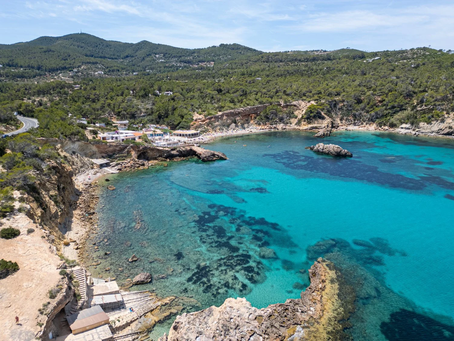 Aerial view of a coastal area featuring clear turquoise waters, rocky shoreline, and a small beach with surrounding greenery.