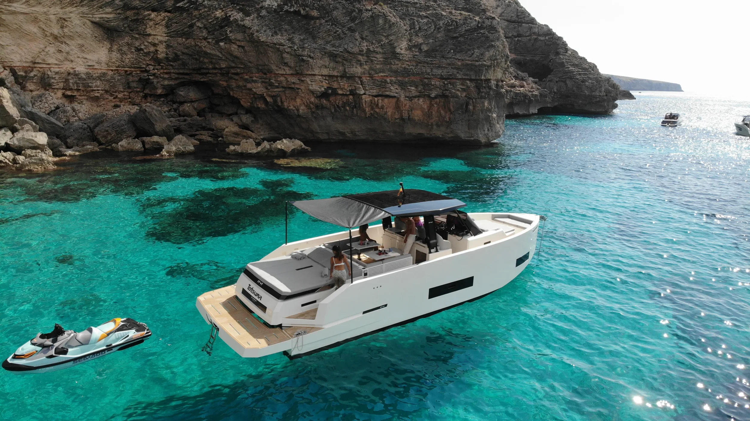 De Antonio 42 Tot Suma cruising over clear turquoise water near rocky Ibiza cliffs.