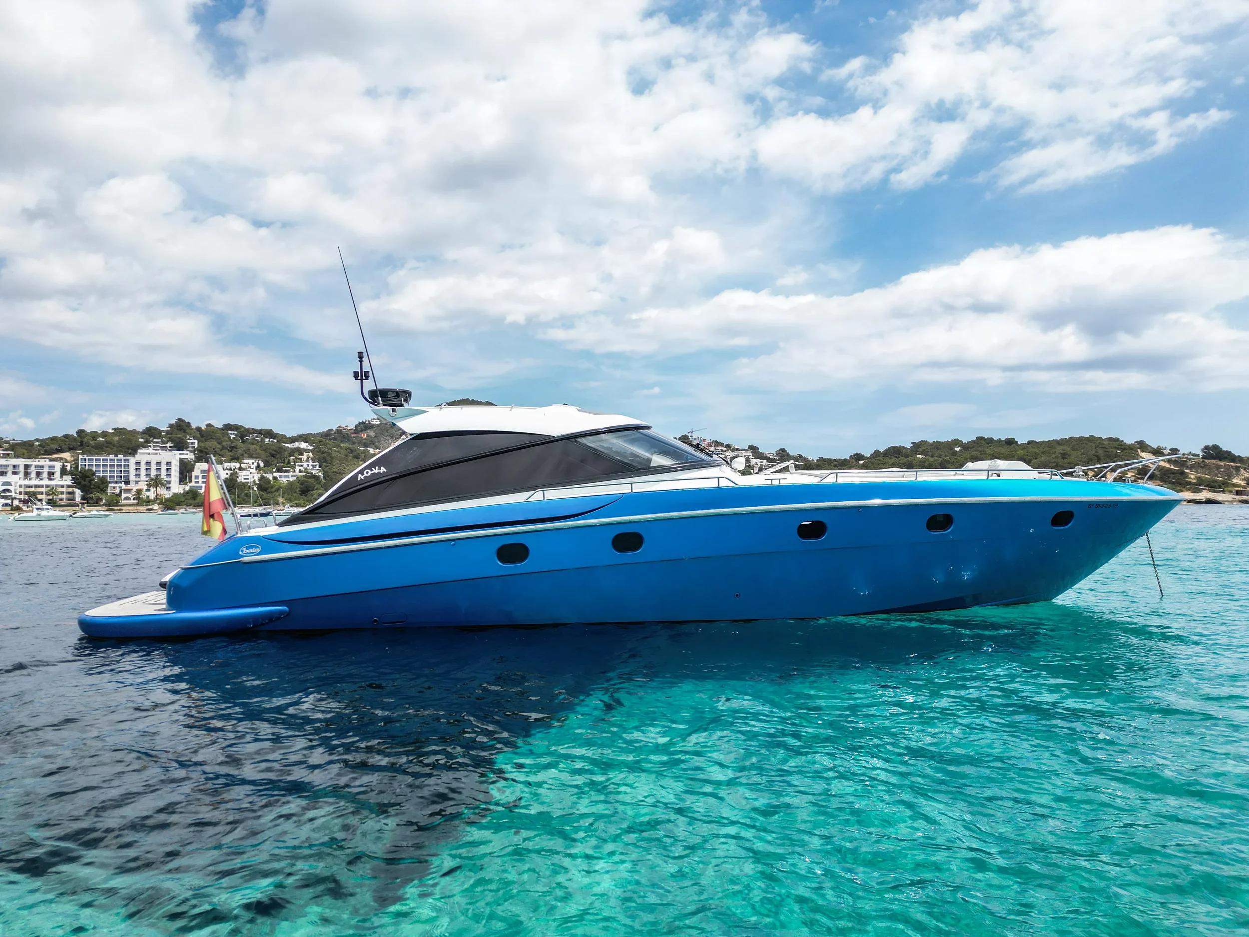 Baia 54 Surreal side profile anchored in clear shallow water with coastal scenery behind.
