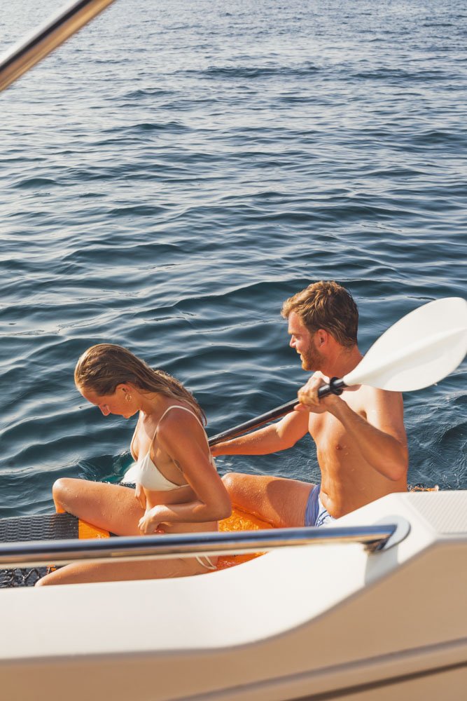 Two people on a boat, one holding a paddle, near the water.