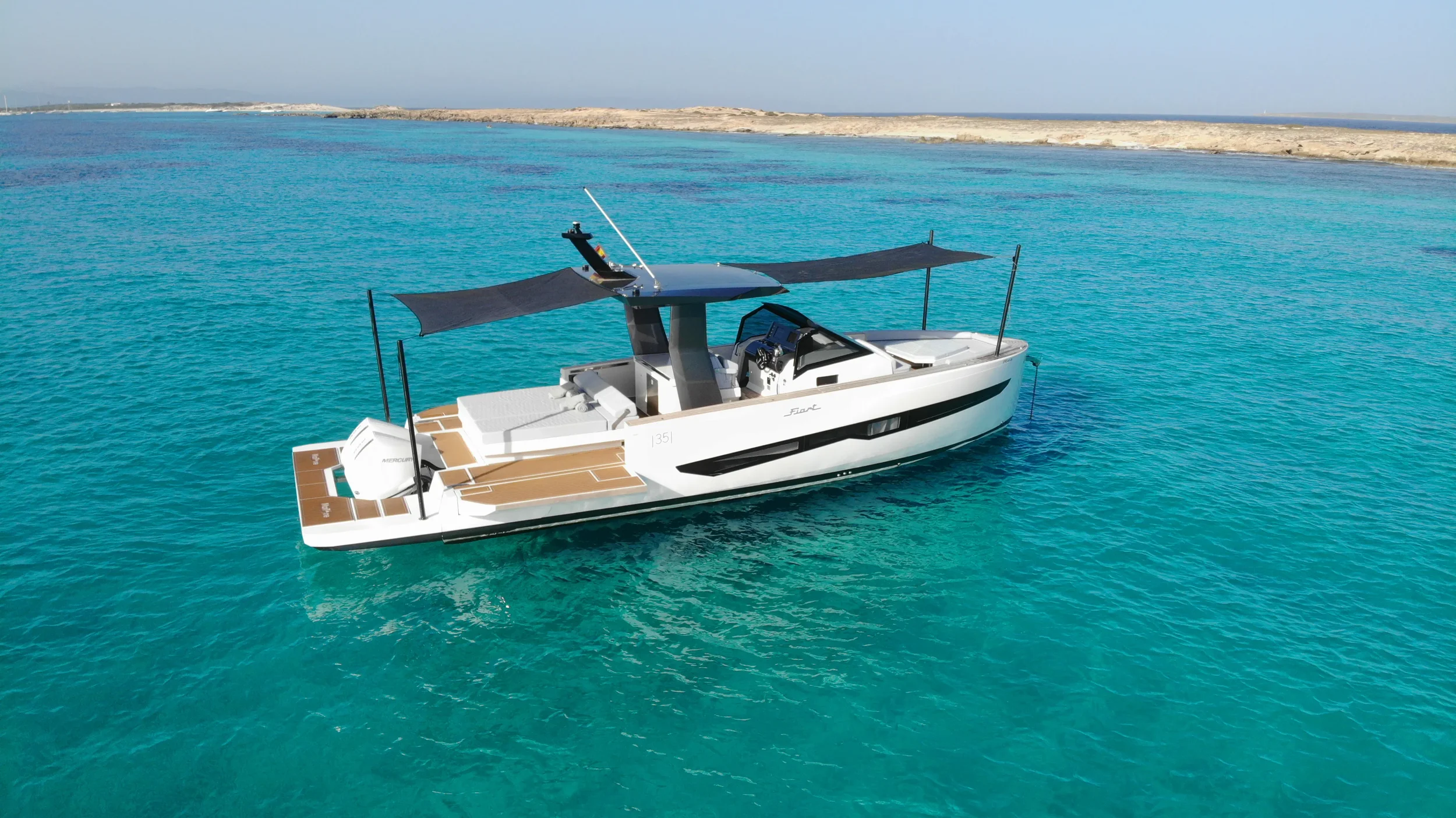 Wide shot of the Fiart 35 Martone W positioned near the shoreline showing the full walk-around deck and sunshade setup.
