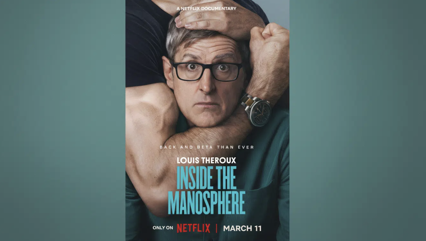 LOUIS THEROUX A WHITE MAN WITH GLASSES BEING HELD IN AN ARM CHOKE BY A MAN WITH BIG MUSCLES