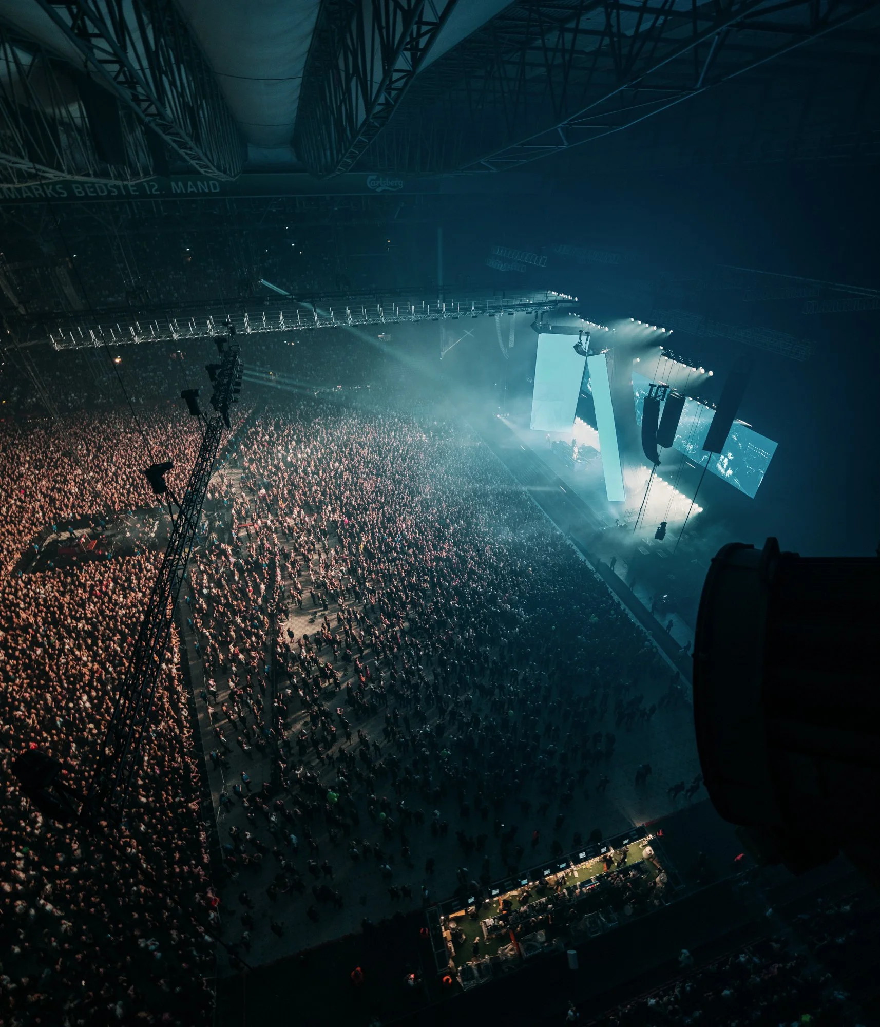 Crowd at a large indoor concert or event with stage lighting and screens