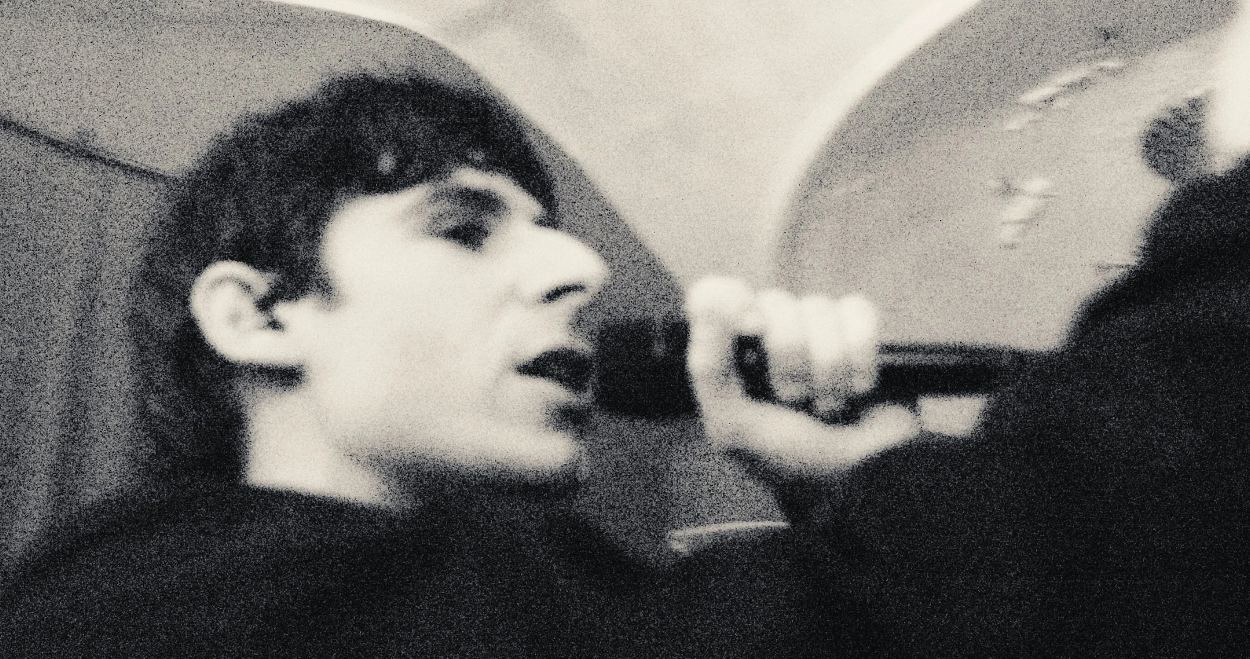 A young person with dark hair singing into a microphone in a black and white photo.