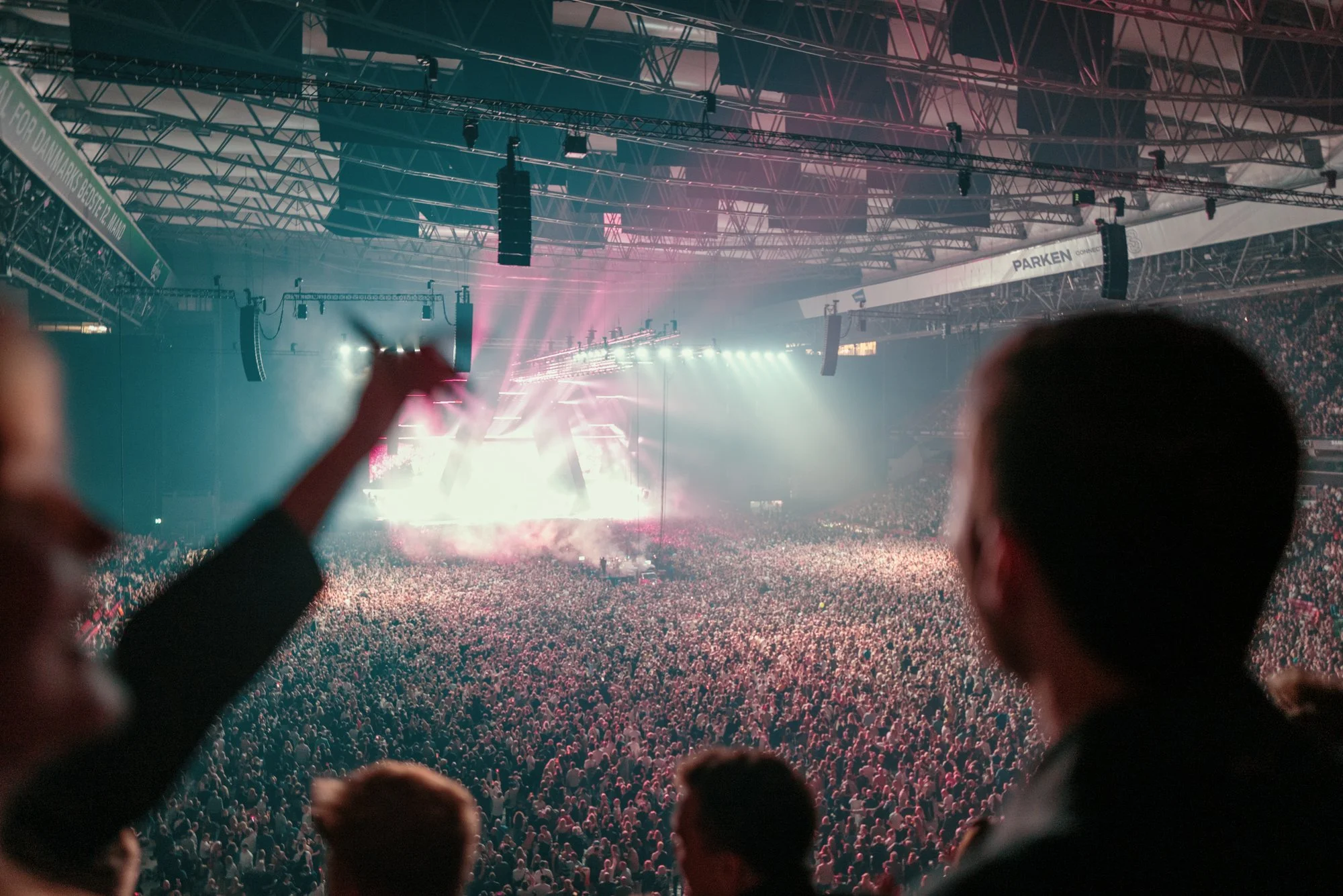 Crowd watching a concert in a large indoor arena with stage lighting.