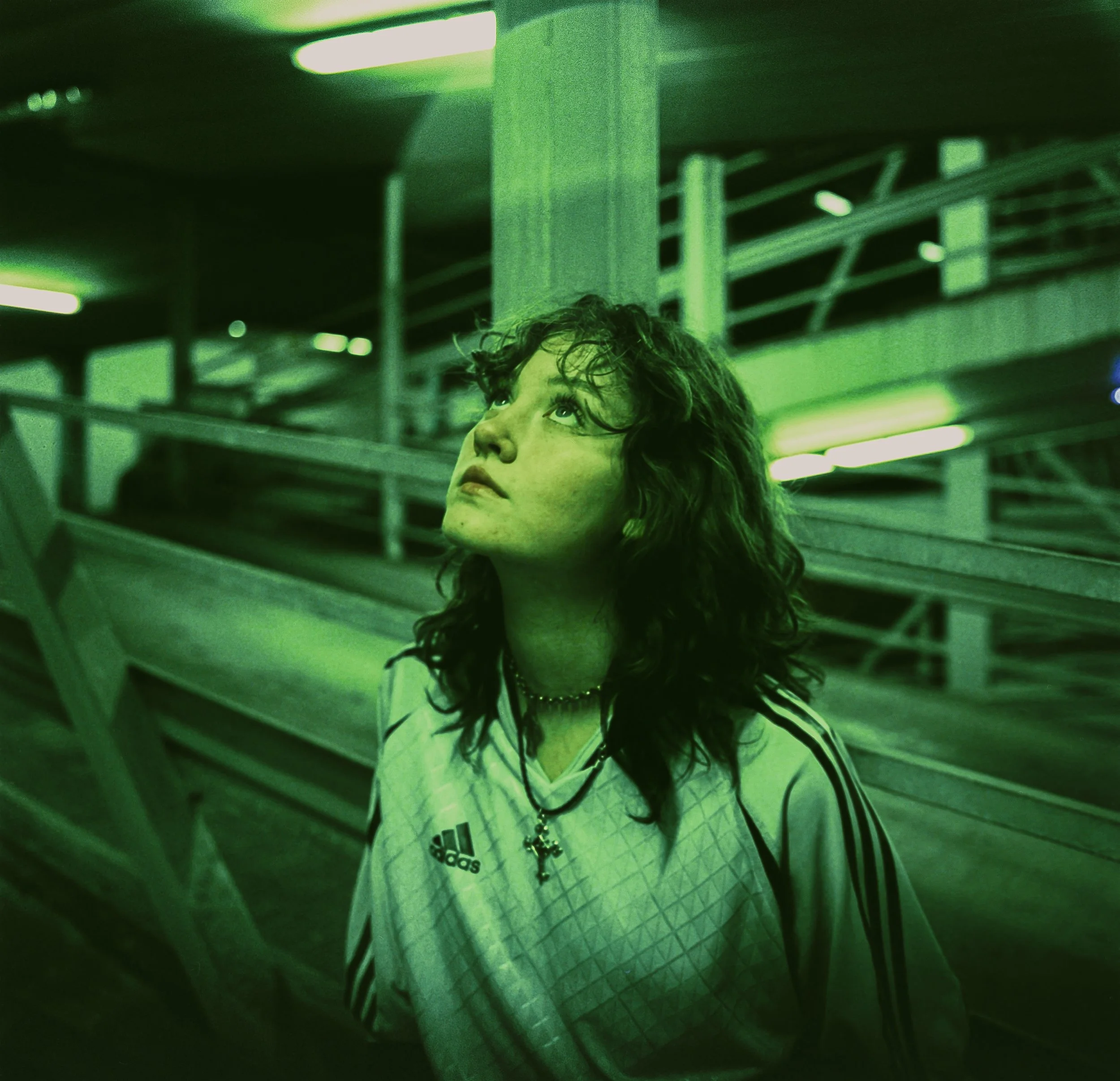 A young woman with curly hair looking up in a dimly lit green-colored parking garage.