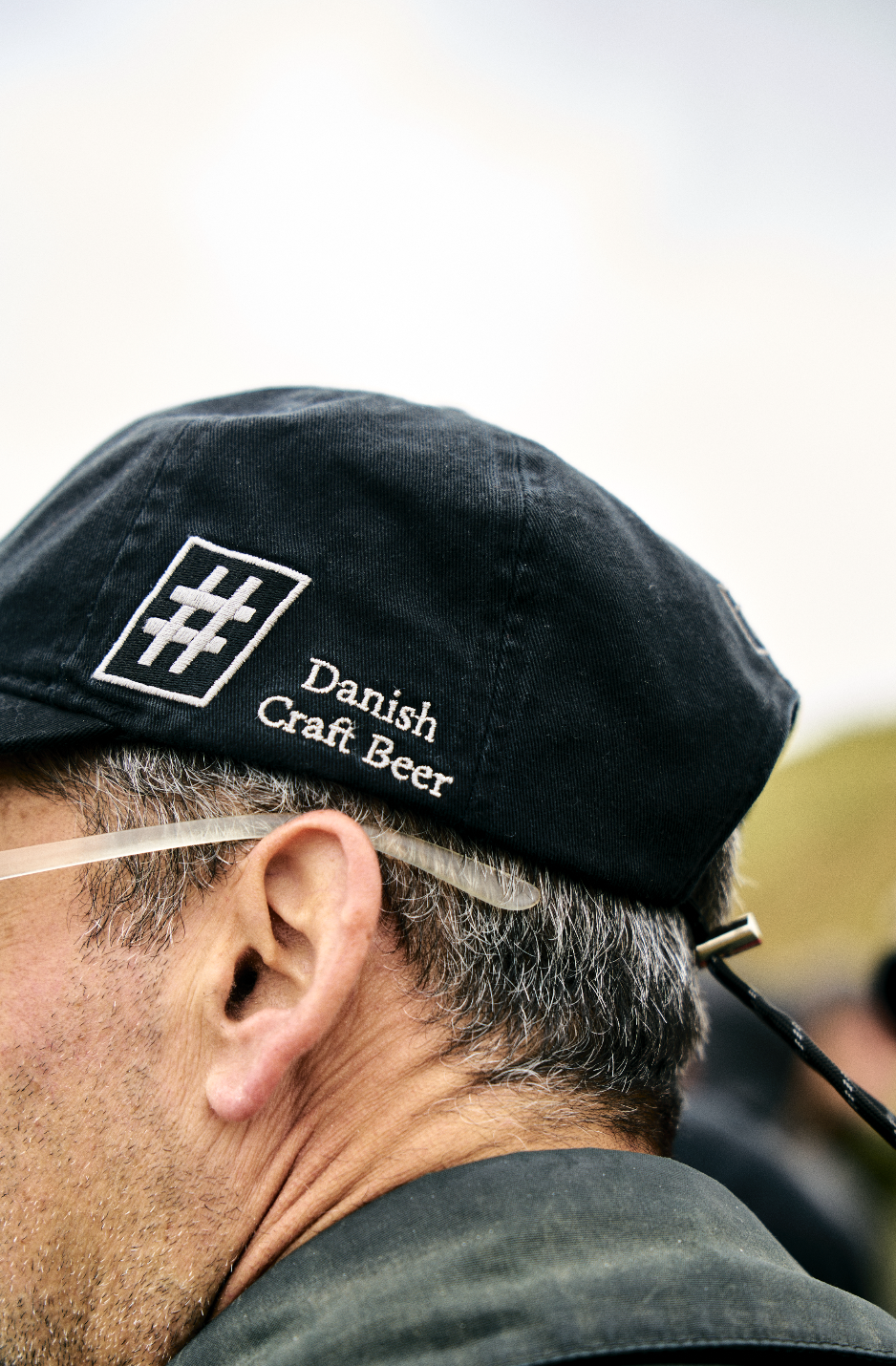 A person wearing a black cap with the logo and text 'Danish Craft Beer' embroidered on it, and glasses, captured from the side.