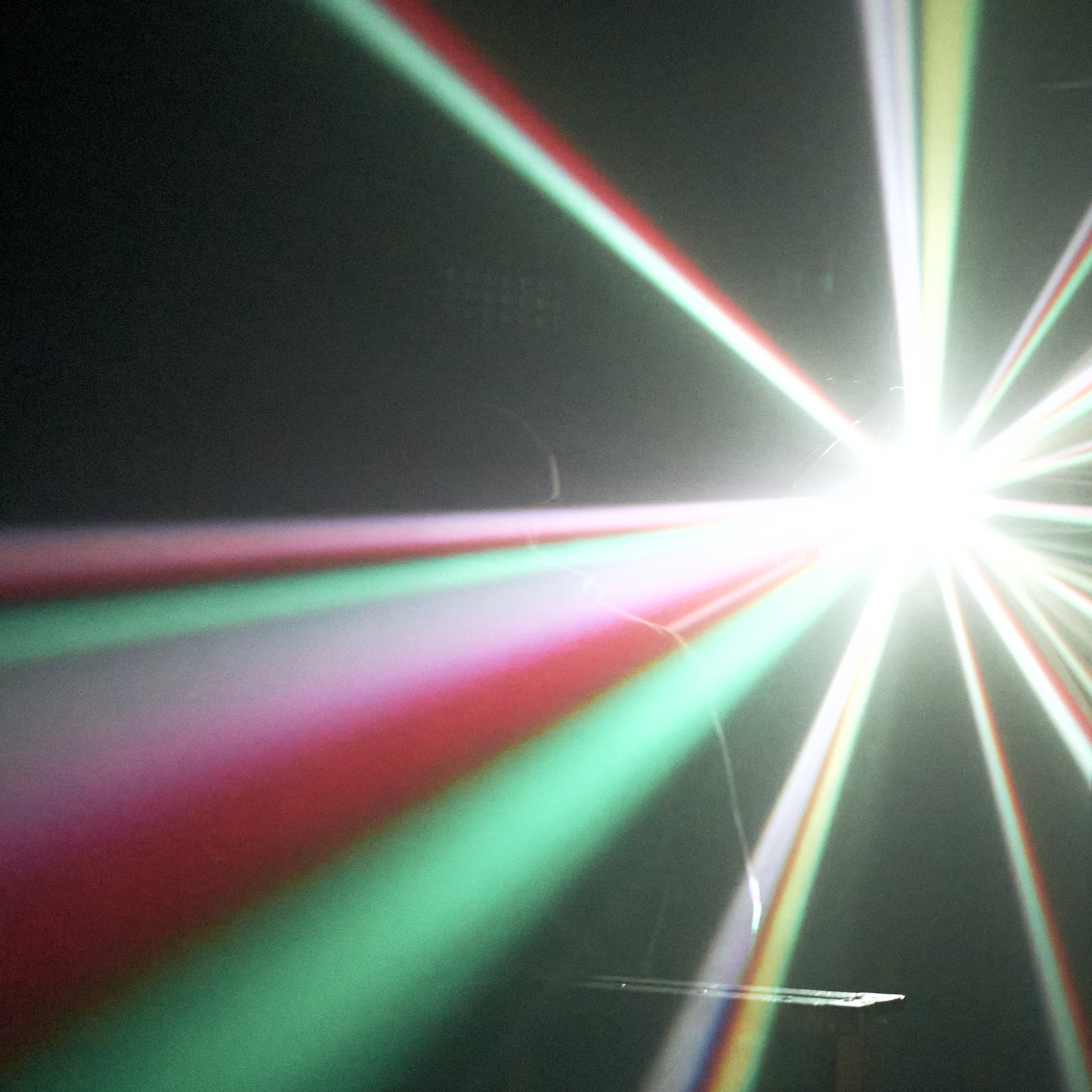 Bright white light with red, green, and blue laser beams radiating outward in a dark setting.