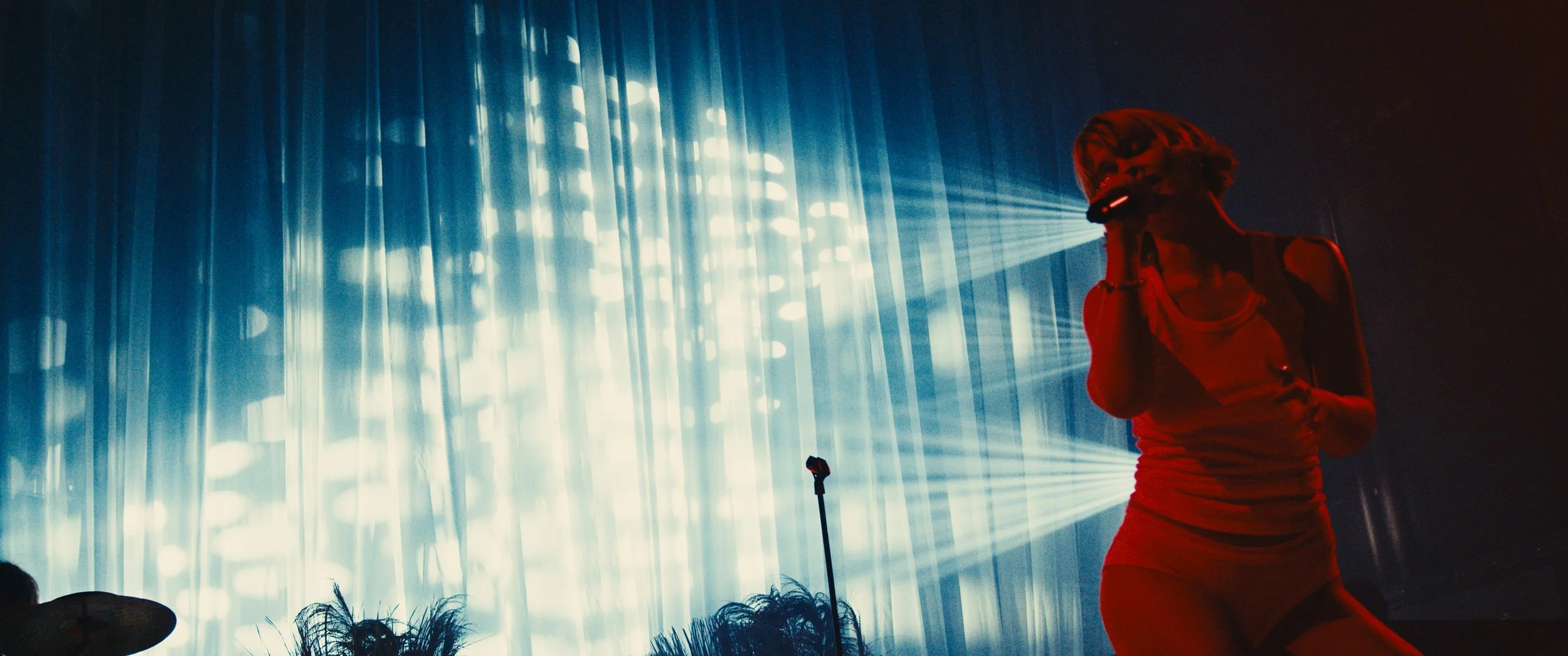 A woman singing on stage with blue stage lights and a microphone stand in the foreground.