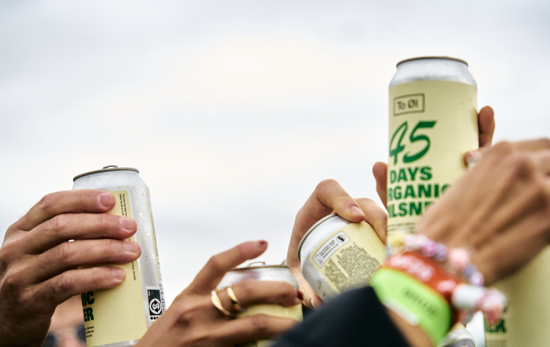 People raising cans of organic sparkling water in a toast outdoors with overcast skies.