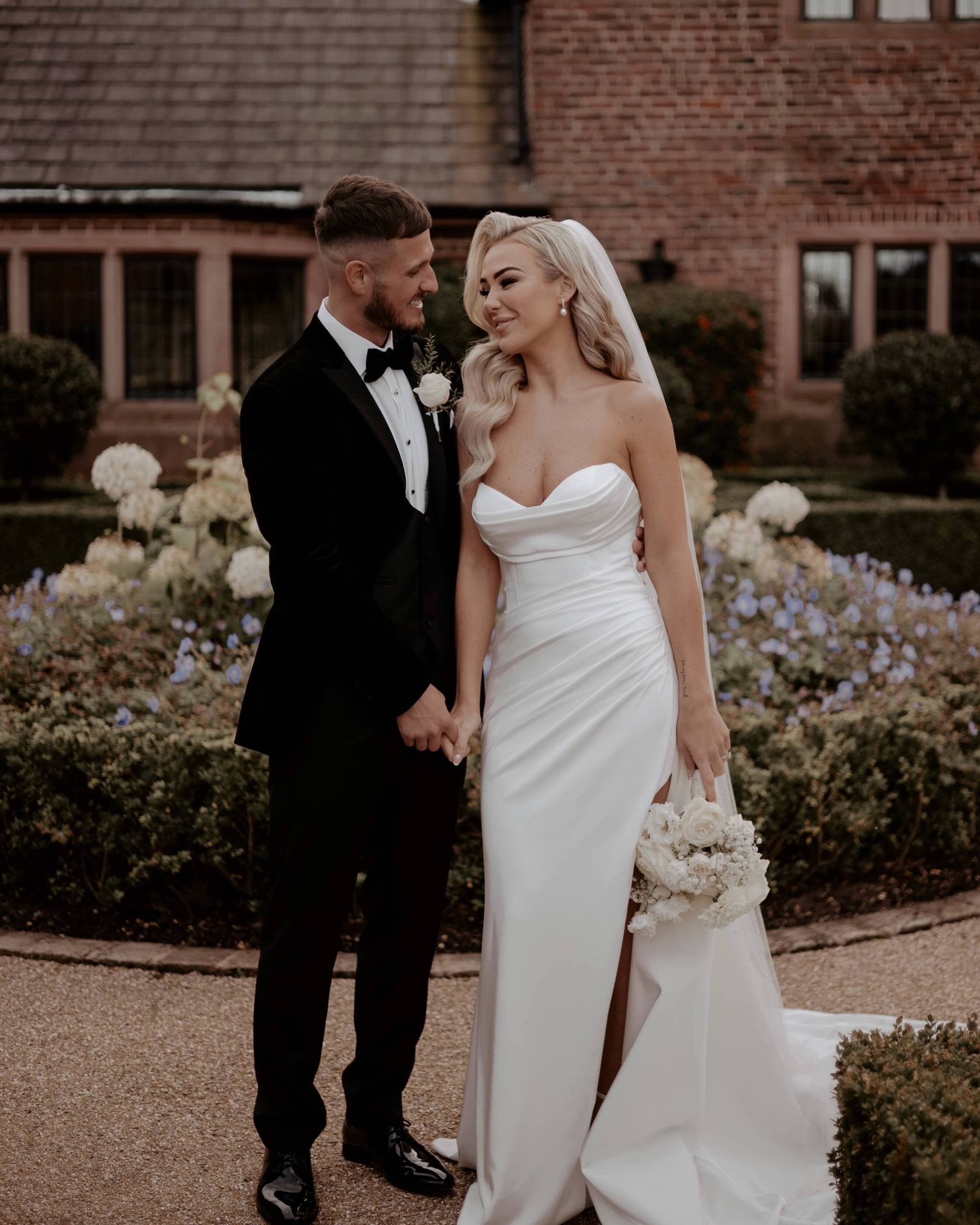 Bride and Groom pose for a photo . Bride is wearing a strapless wedding dress and natural wedding makeup