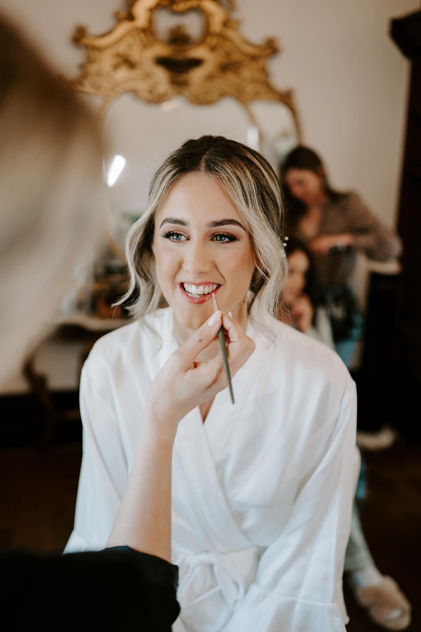 Bride is having her wedding makeup done. The makeup artist adds her lipstick.