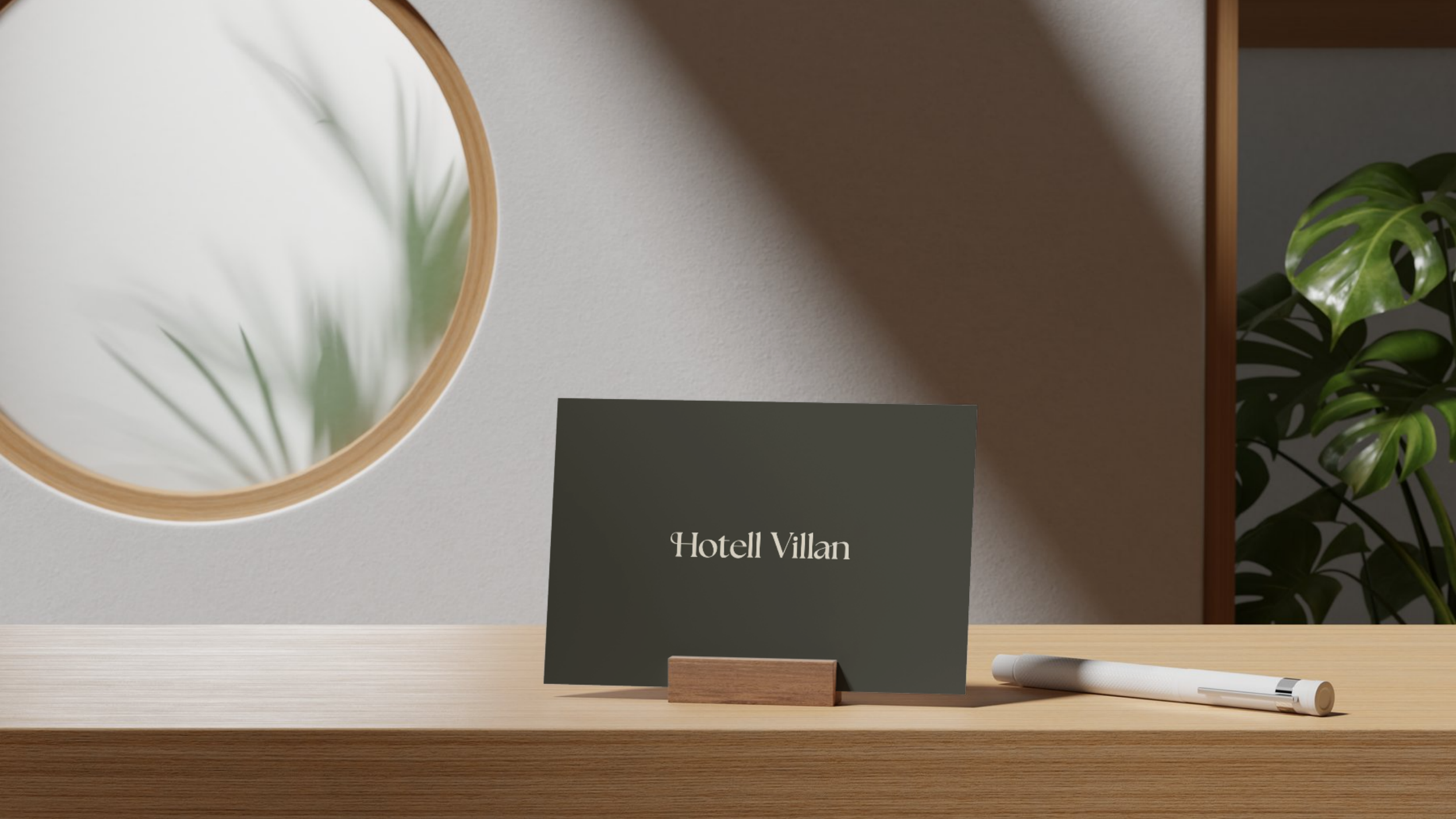 Mörkgrått bordskort med Hotell Villans logotyp på ett träbord, med en rund spegel och en grön växt i bakgrunden.