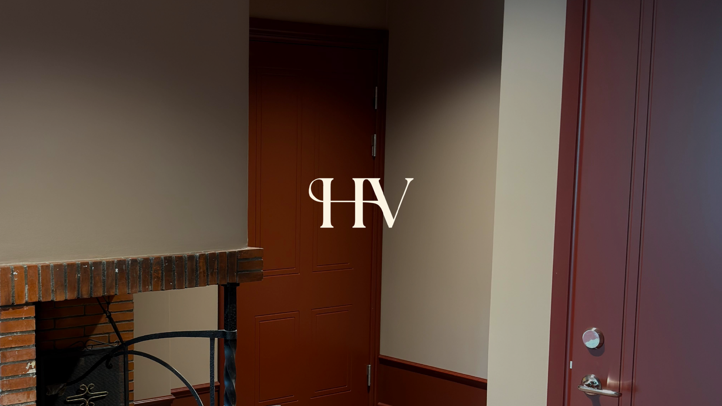 Hotell Villans monogram HV i vitt över en bild av en hotellkorridor med röda dörrar och en tegelspis.