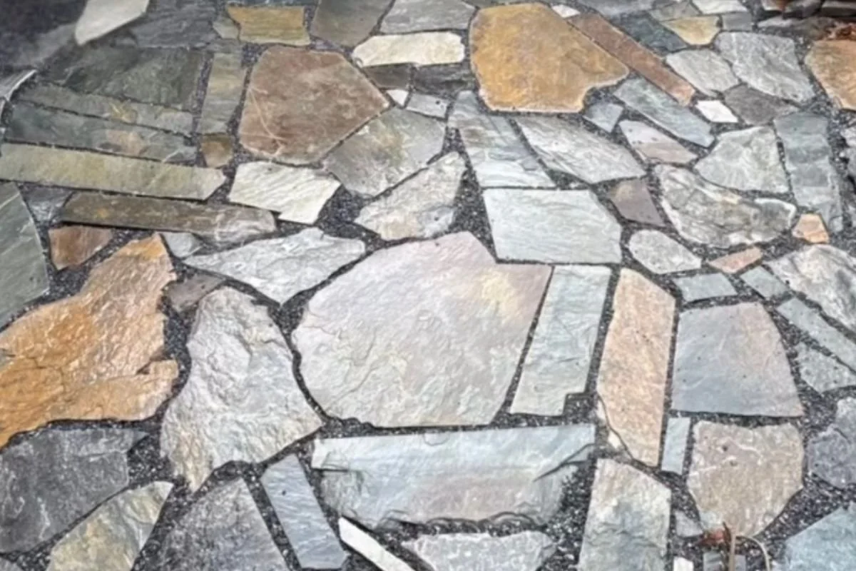 Close-up of a stone patio with irregularly shaped stones in shades of gray, brown, and tan, fitted together with black grout.