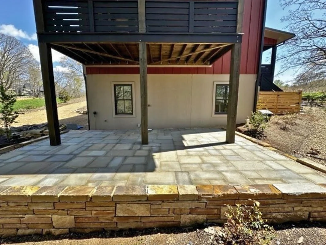 Customer Pennsylvania Blue Thermal stone patio featuring clean, rectangular stone slabs with a smooth finish. The patio is installed under a covered porch area and bordered by a natural stacked stone retaining wall; a modern and durable space