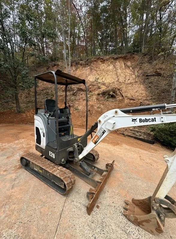 Mini excavator grading and resloping hillside property for retaining wall installation in Western North Carolina
