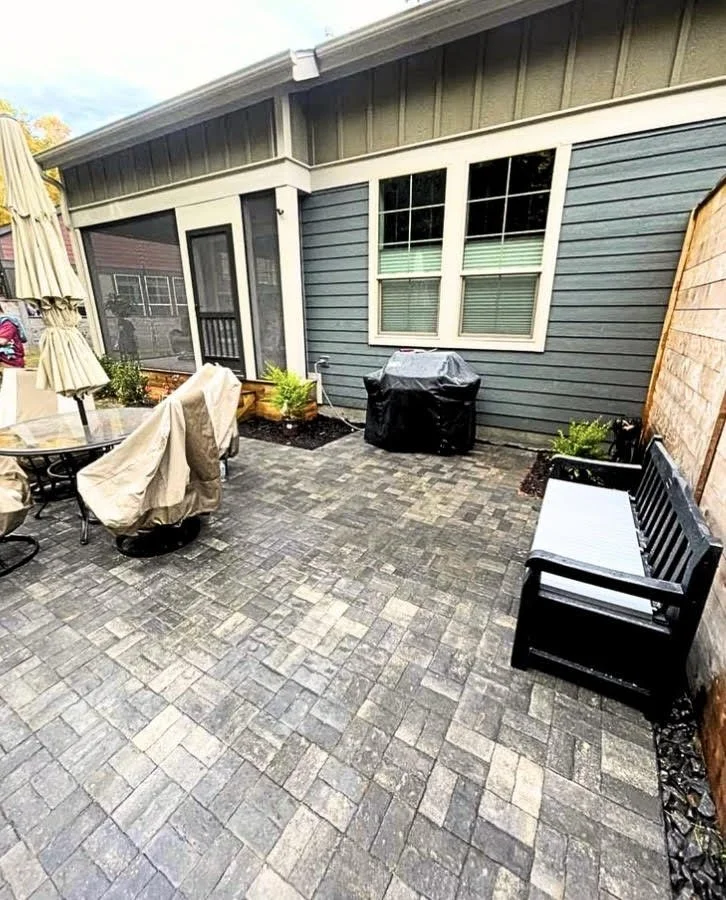 Backyard paver patio with a herringbone pattern beside a home.