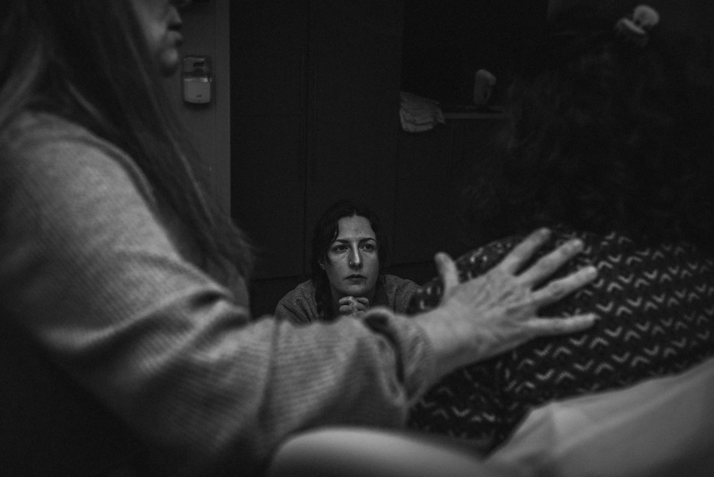  Ale kneels in the center of the photo, with her hands clasped and resting under her chin. The light catches her face, which is calm as she looks forward, watching Lucy. She is framed by Meg and Lucy, both facing away from the camera. Meg’s hand is r