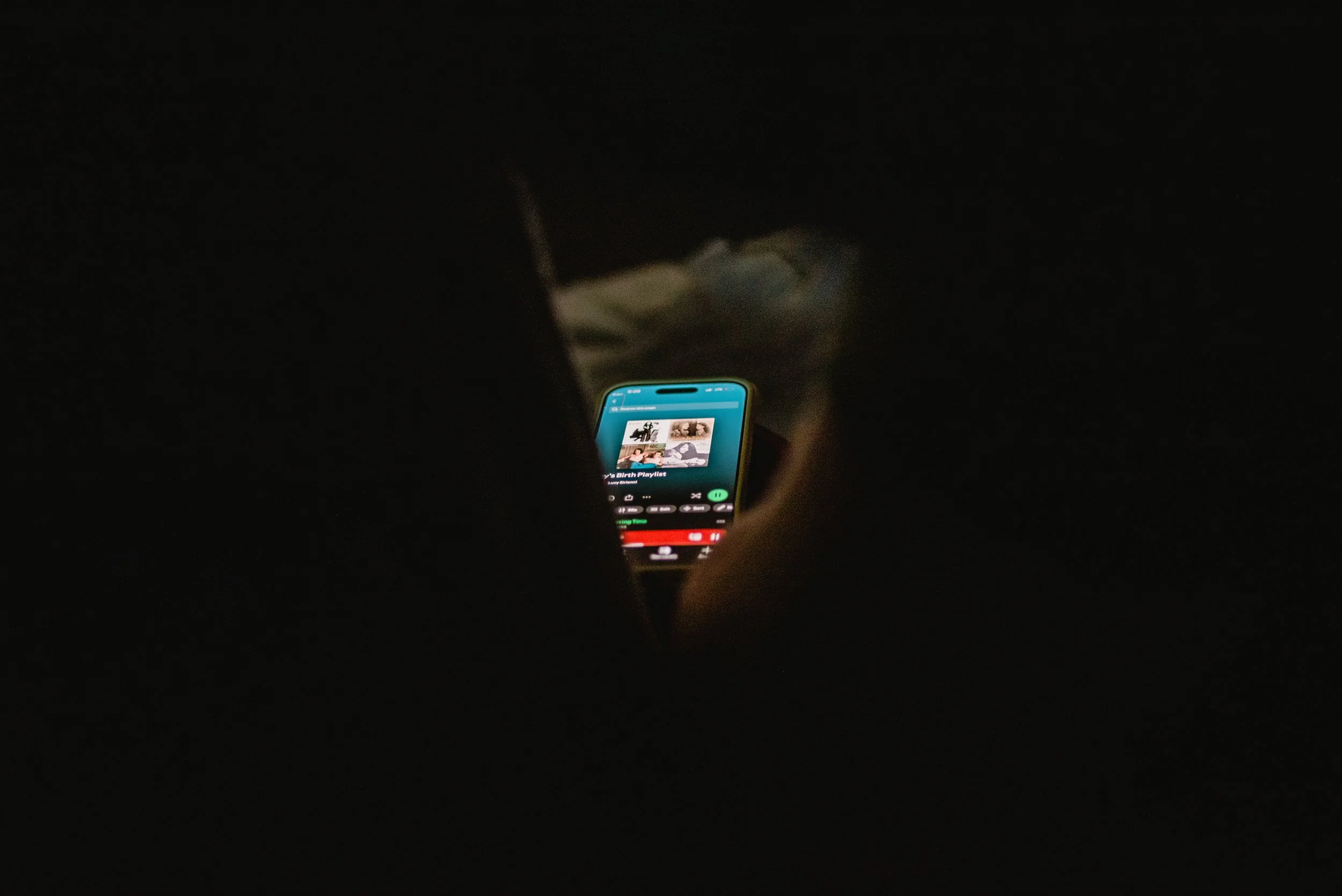  A phone sits in the center of the image, the screen lit up with Lucy’s birth playlist. The phone is just visible through a triangle-shaped gap between two people’s shoulders. 