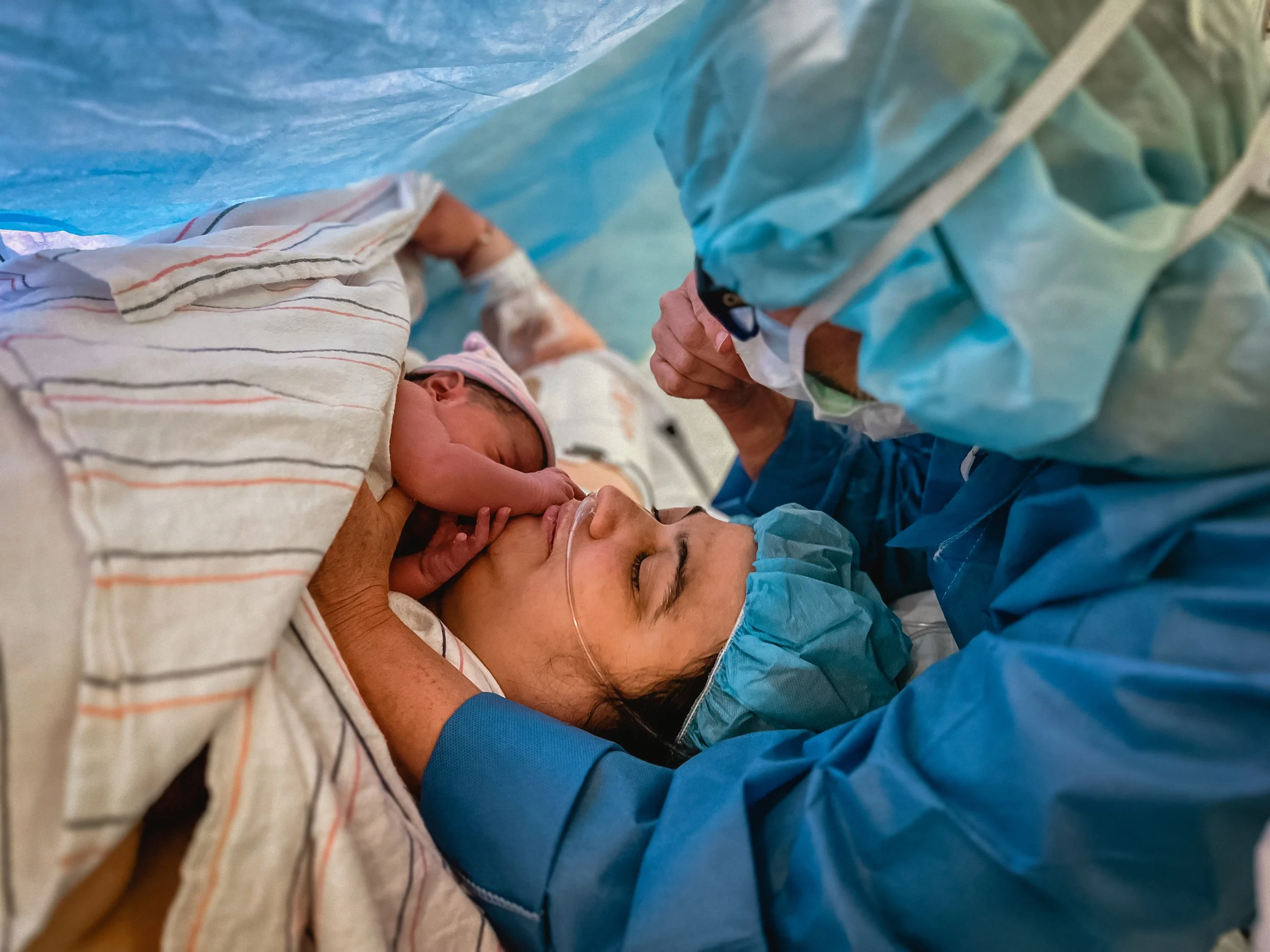  Lucy is at the center of the image, peace and calm across her face. Her newborn daughter Beatrice is held to her chest, her small hand resting on Lucy’s face. Meg rest her arms on the operating table, helping to hold Beatrice to Lucy, one hand comin