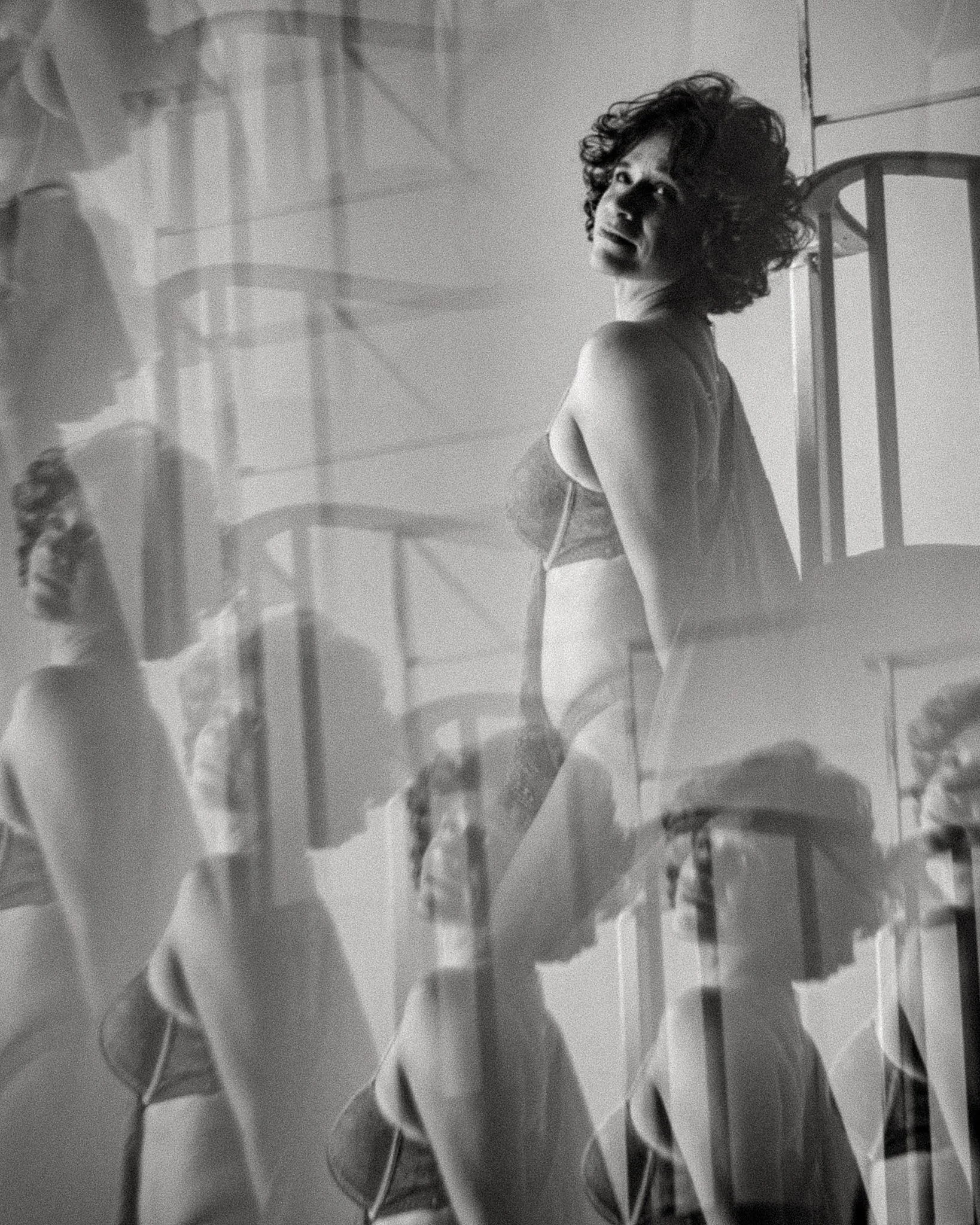 Una mujer con cabello rizado en ropa interior, posando en un ambiente con reflejos y múltiples exposiciones en la fotografía en blanco y negro.