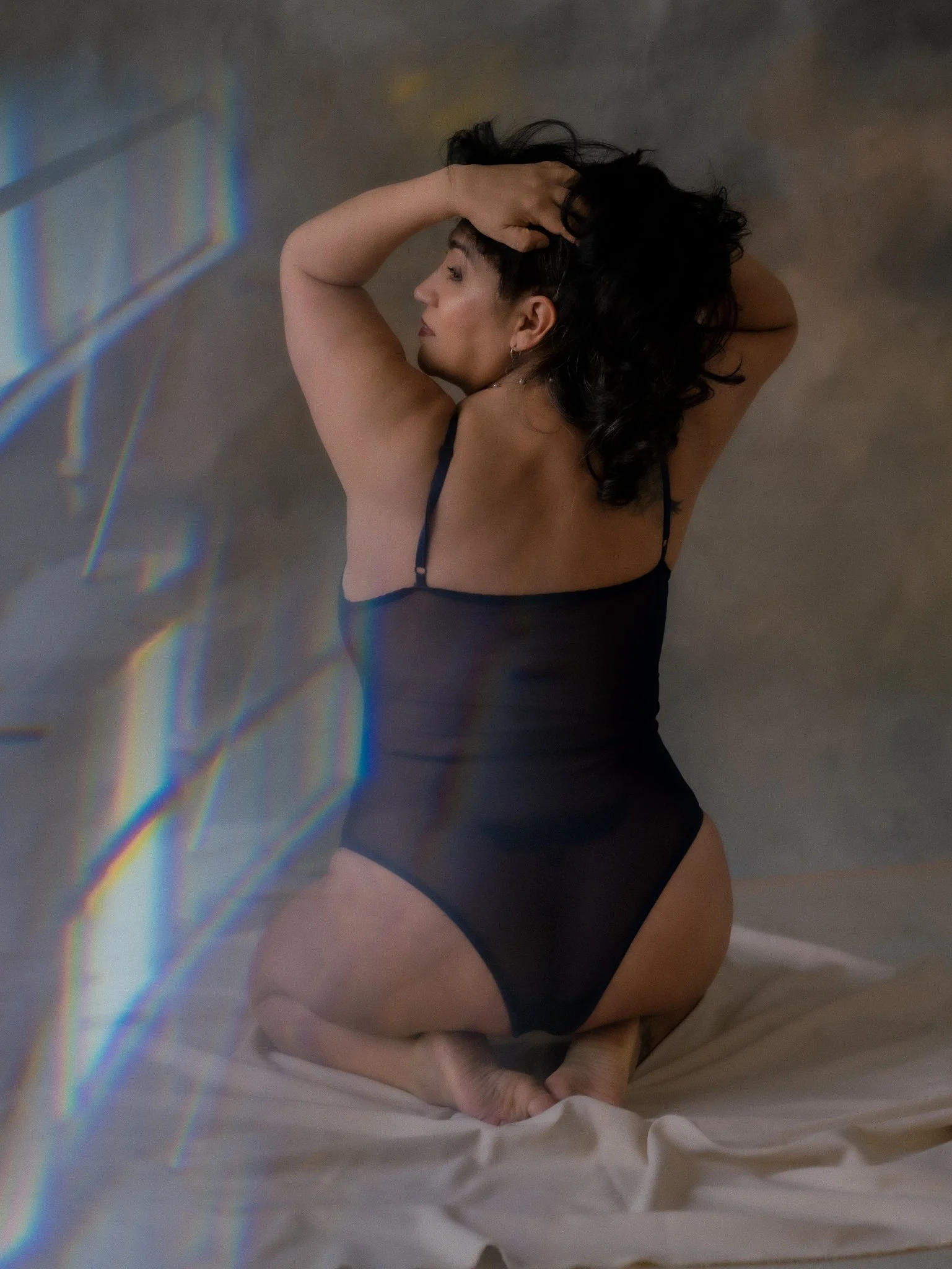 Mujer en lencería negra posando en una postura de articulación con las manos en la cabeza.