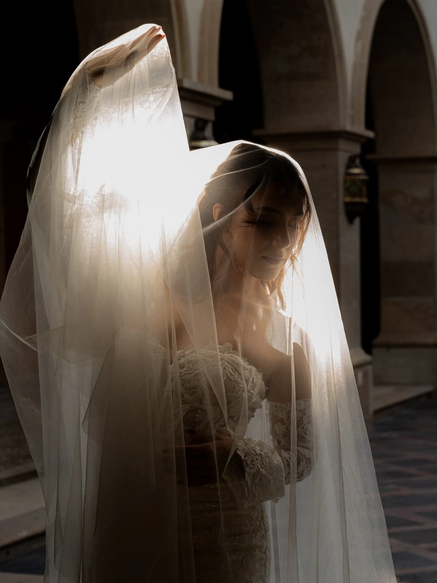 Mujer con vestido de novia y velo, de espaldas, en una iglesia, con luz solar brillante detrás.