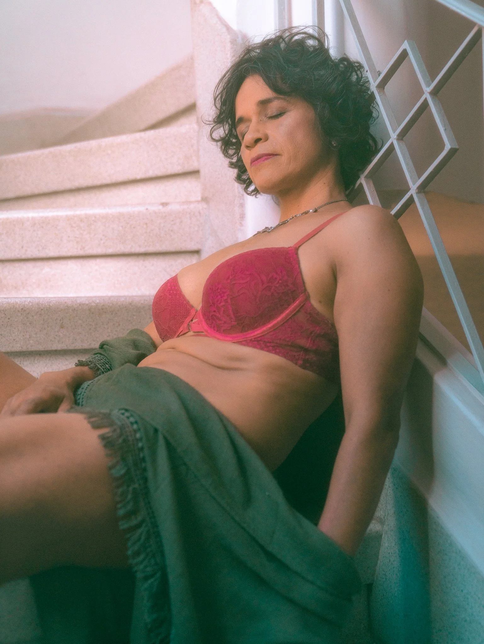 Mujer con cabello rizado, con sujetador rosado y pantalones cortos, descansando en unas escaleras