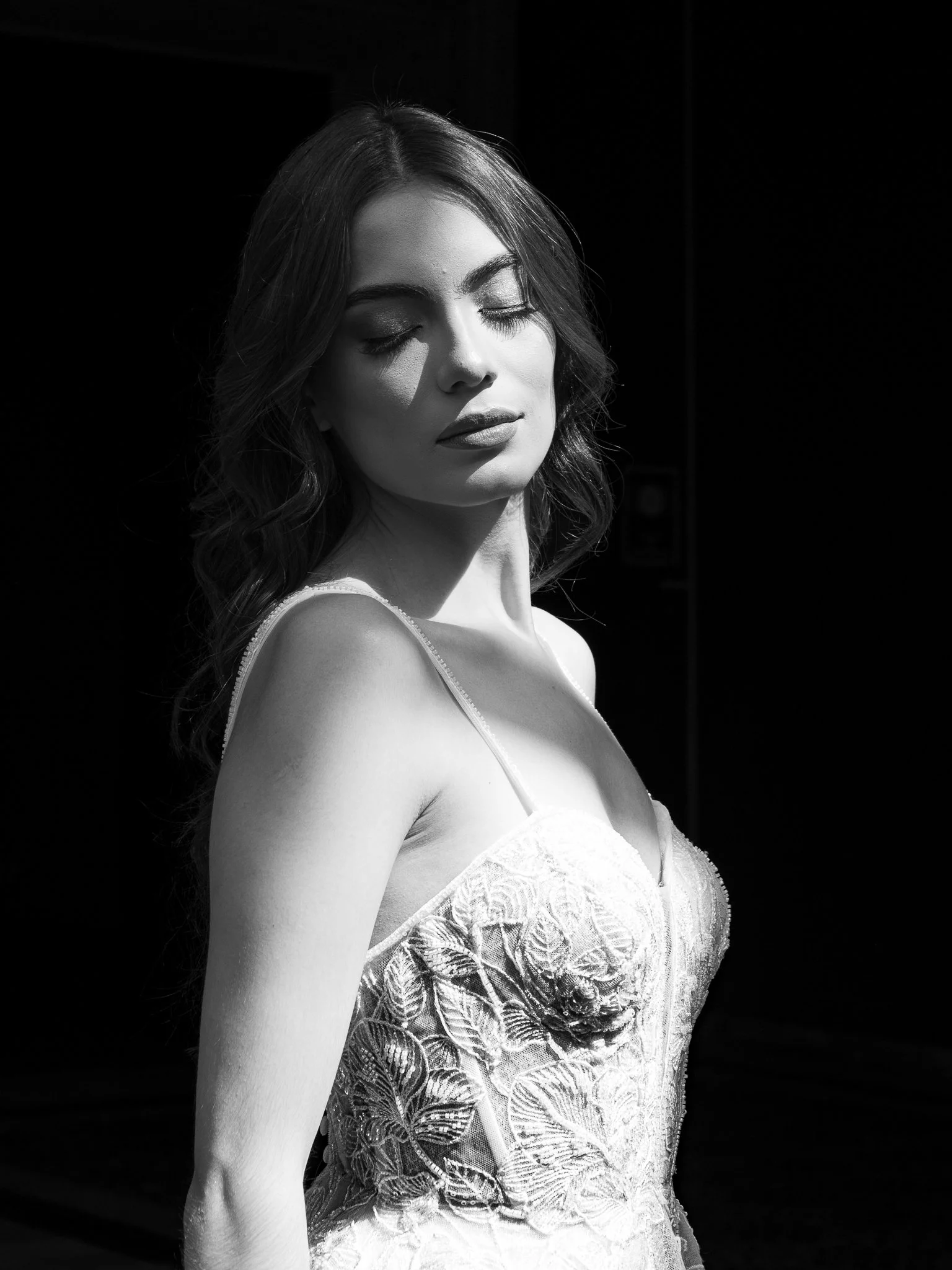 Retrato en blanco y negro de una mujer con ojos cerrados, cabello rizado y vestido de encaje con detalles florales.