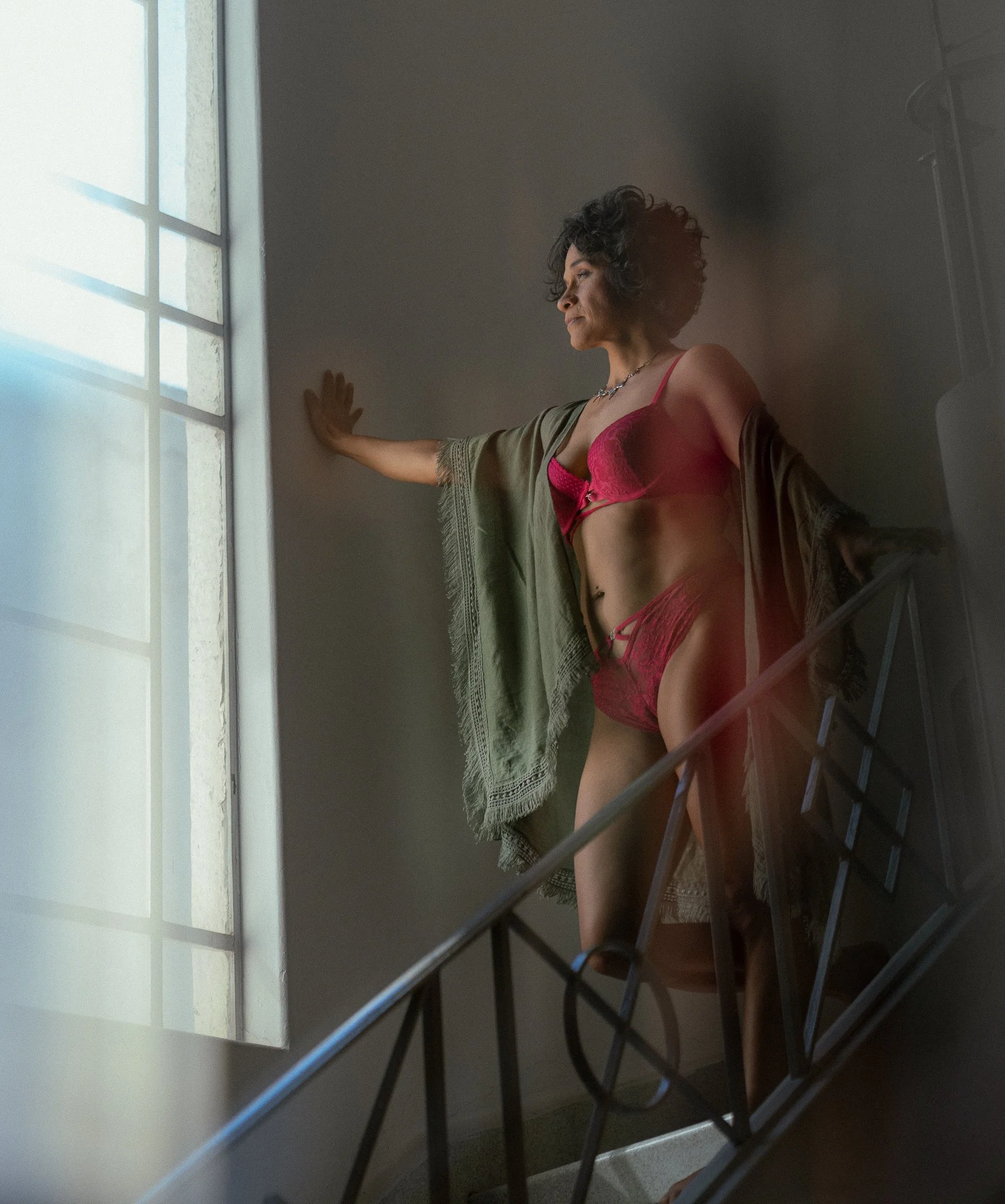 Mujer posando en escaleras cerca de una ventana, viste ropa interior rosa y una manta verde
