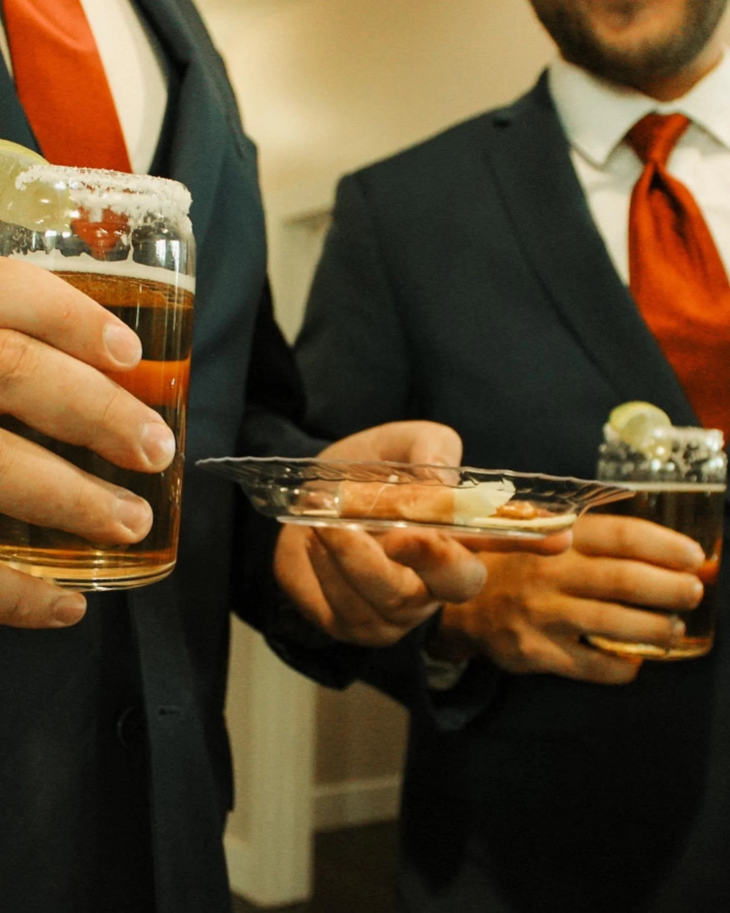 Two people in suits holding drinks, one with a salted rim, and a plate with limes and salt. Focus on hands and attire.
