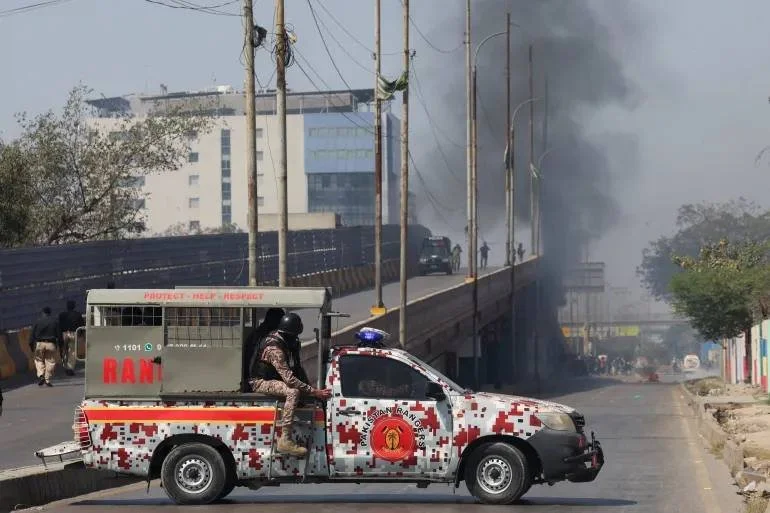Armed security forces vehicle deployed amid smoke and civil unrest, illustrating the threat environment prompting the State Department's worldwide embassy security review following Iran-linked attacks on US facilities