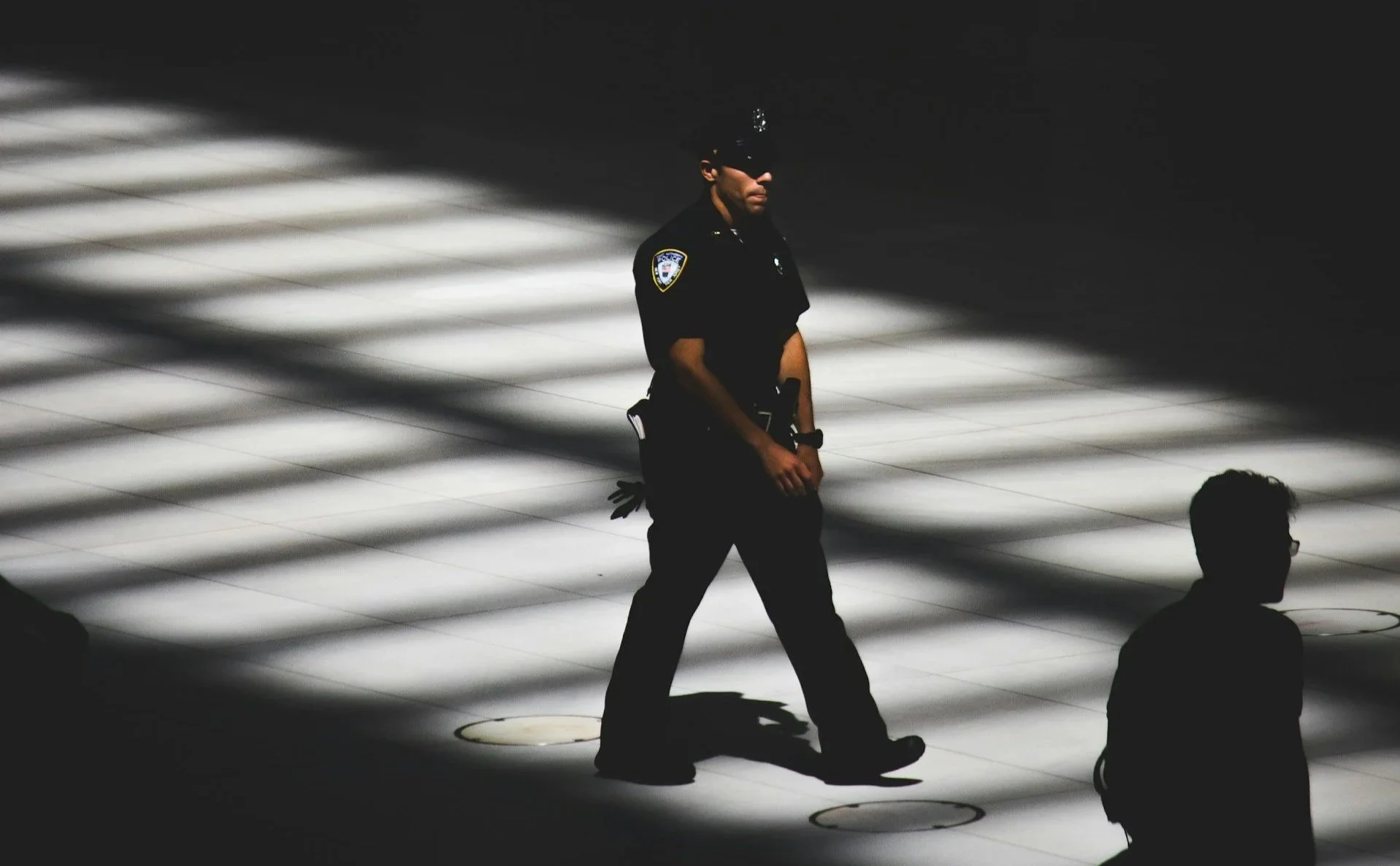 Police officer walking through a shadowed corridor, representing vigilance and threat assessment in public safety work