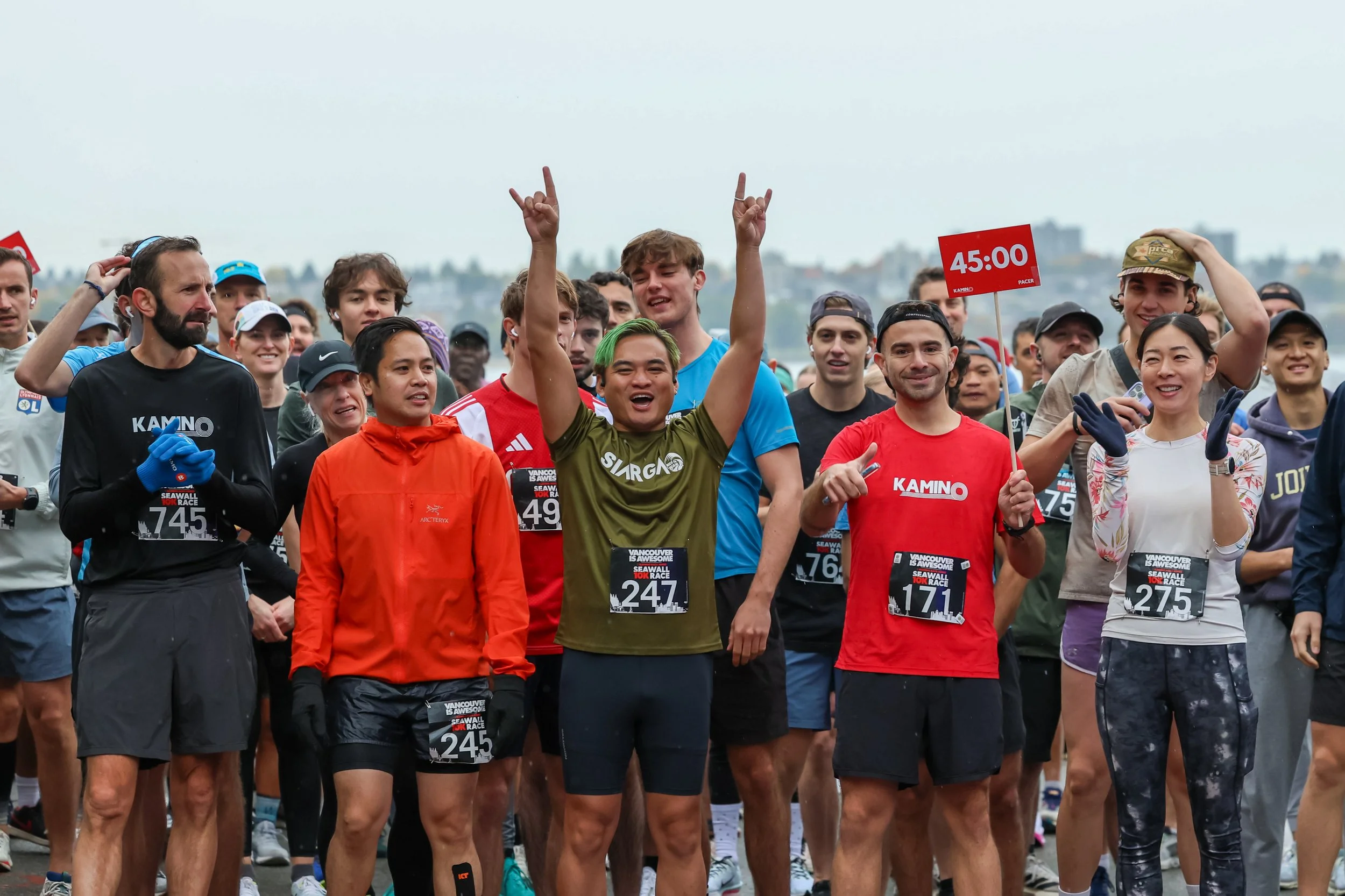 Group of marathon runners at the starting line, some cheering and smiling, with a person holding a sign showing 45:00 minutes