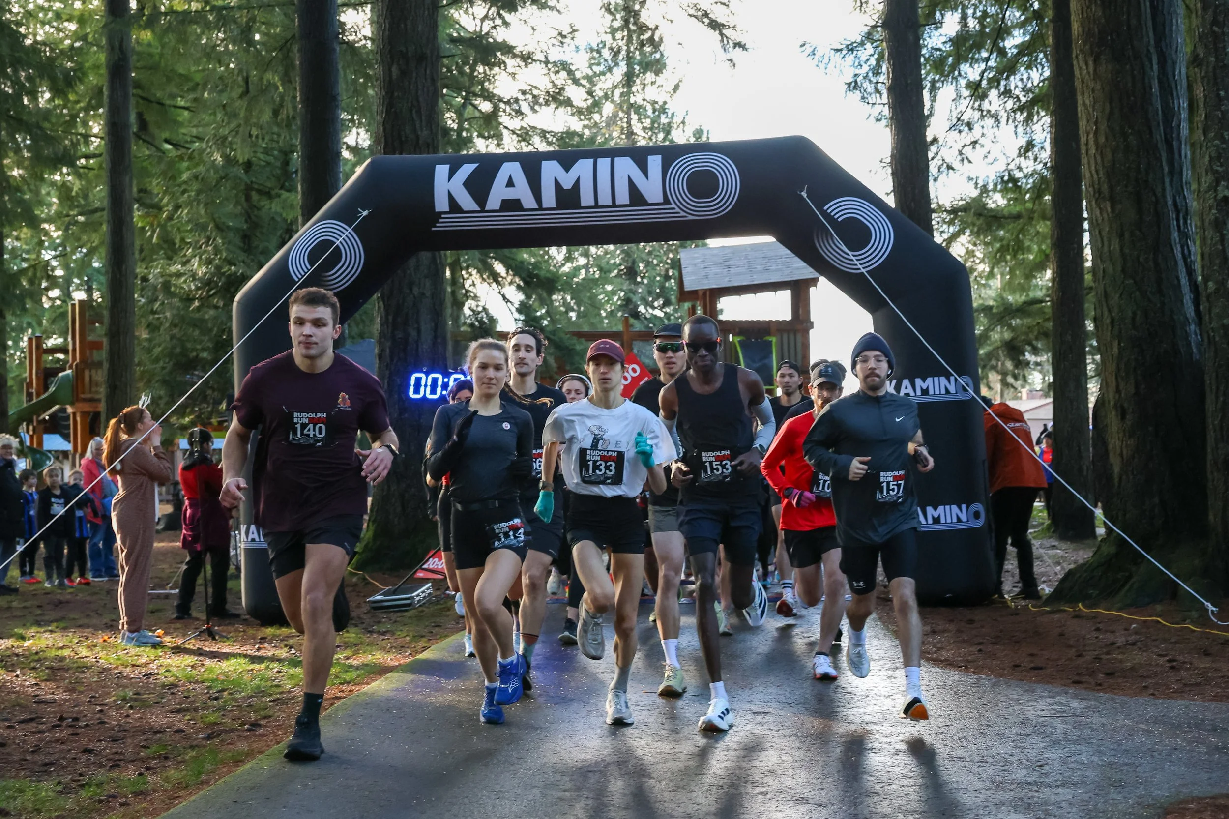 A group of runners starting a race under an archway in a wooded park.