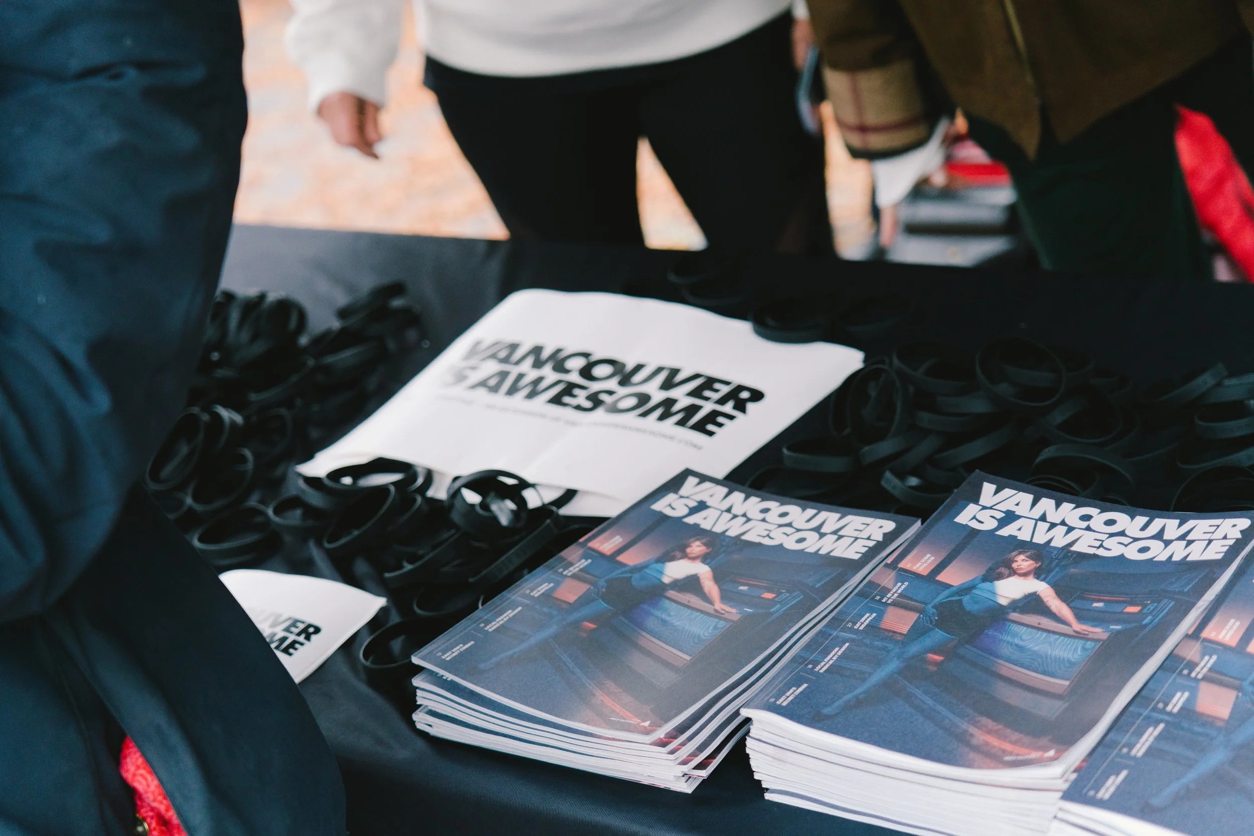 Vancouver is Awesome promotional materials including brochures and black wristbands on a table at an event.