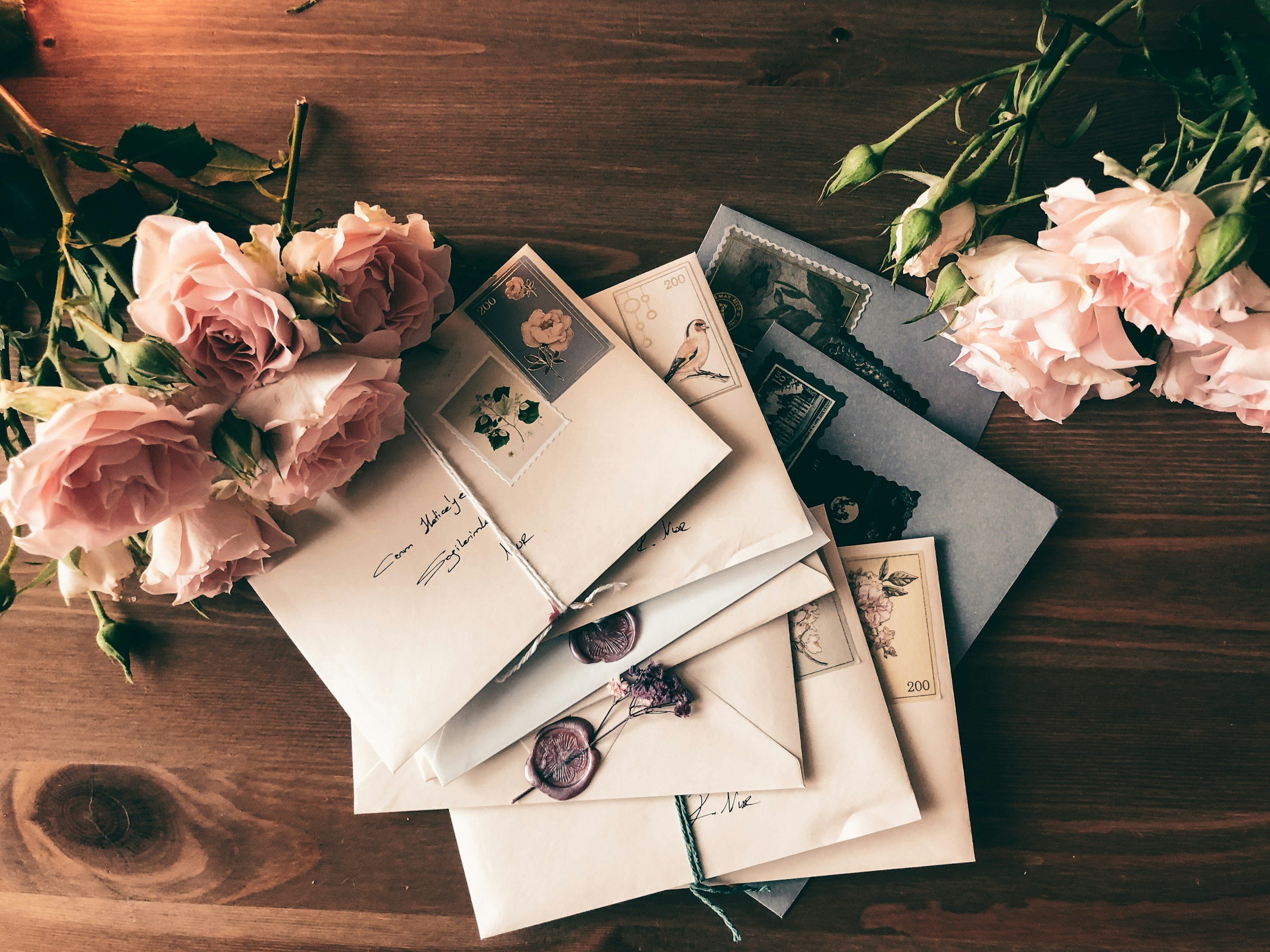 Open envelopes with vintage stamps on a wooden surface, pink roses on either side