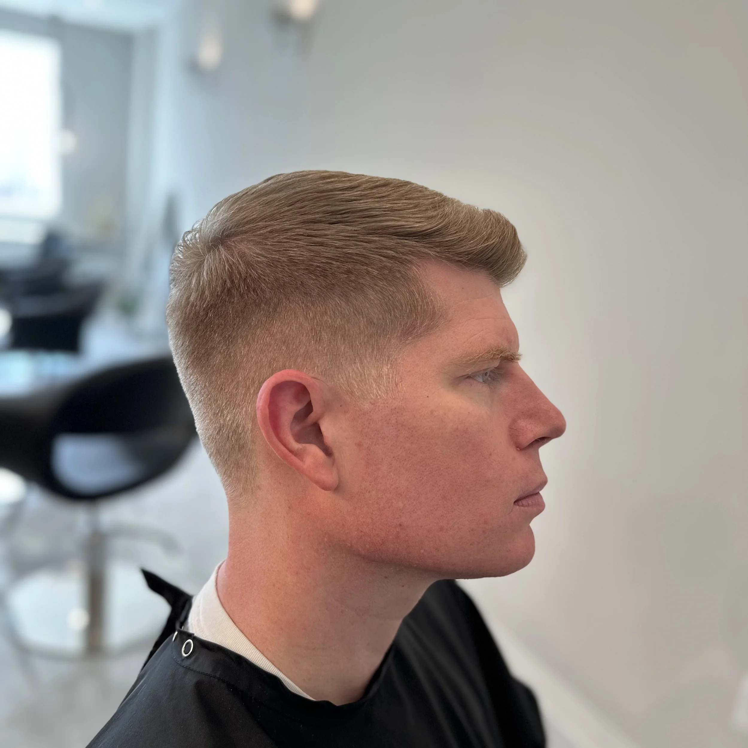 Side profile of a young man with a freshly cut hairstyle at a haircutting salon.