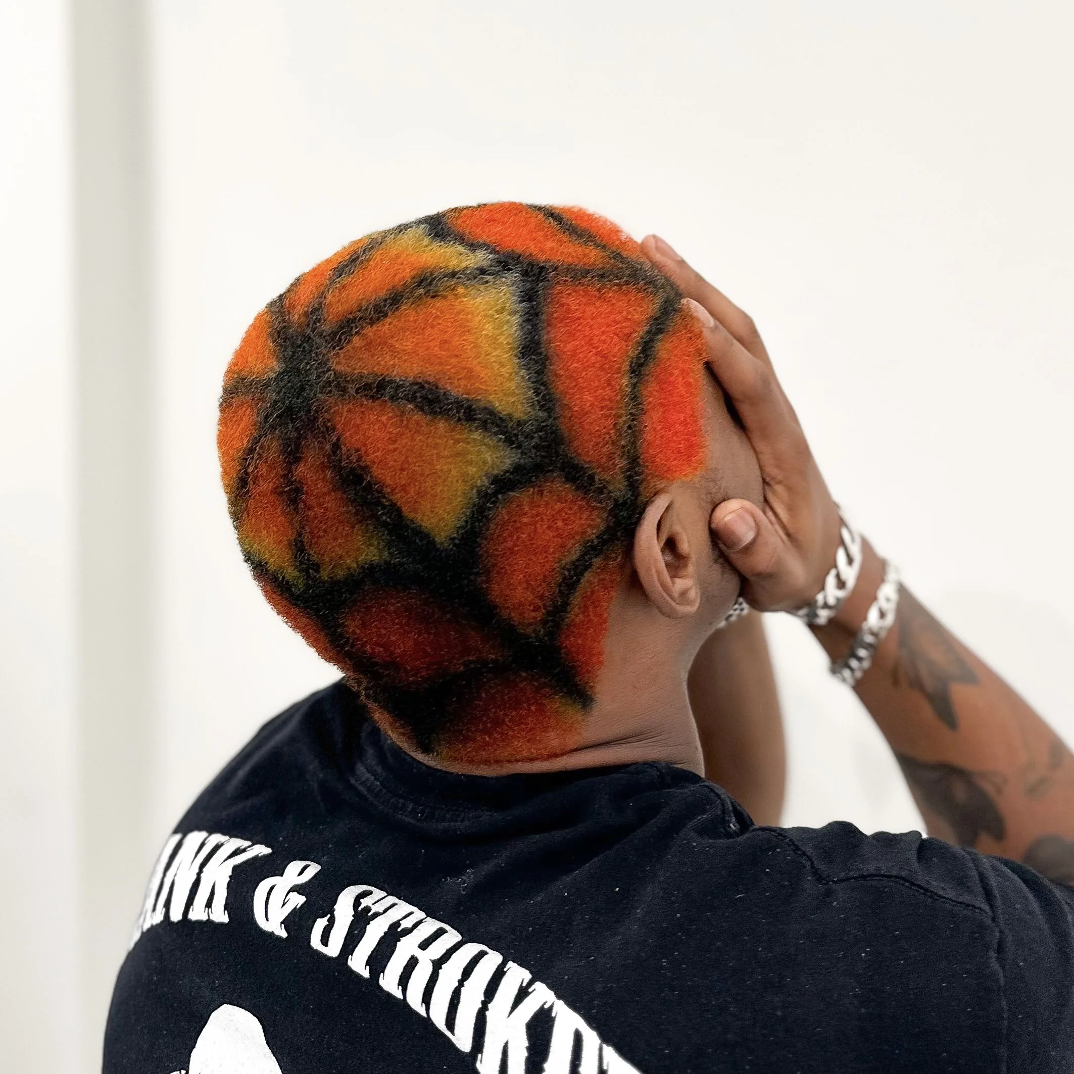 Person with a shaved head featuring a basketball design painted with black lines and orange and yellow sections.